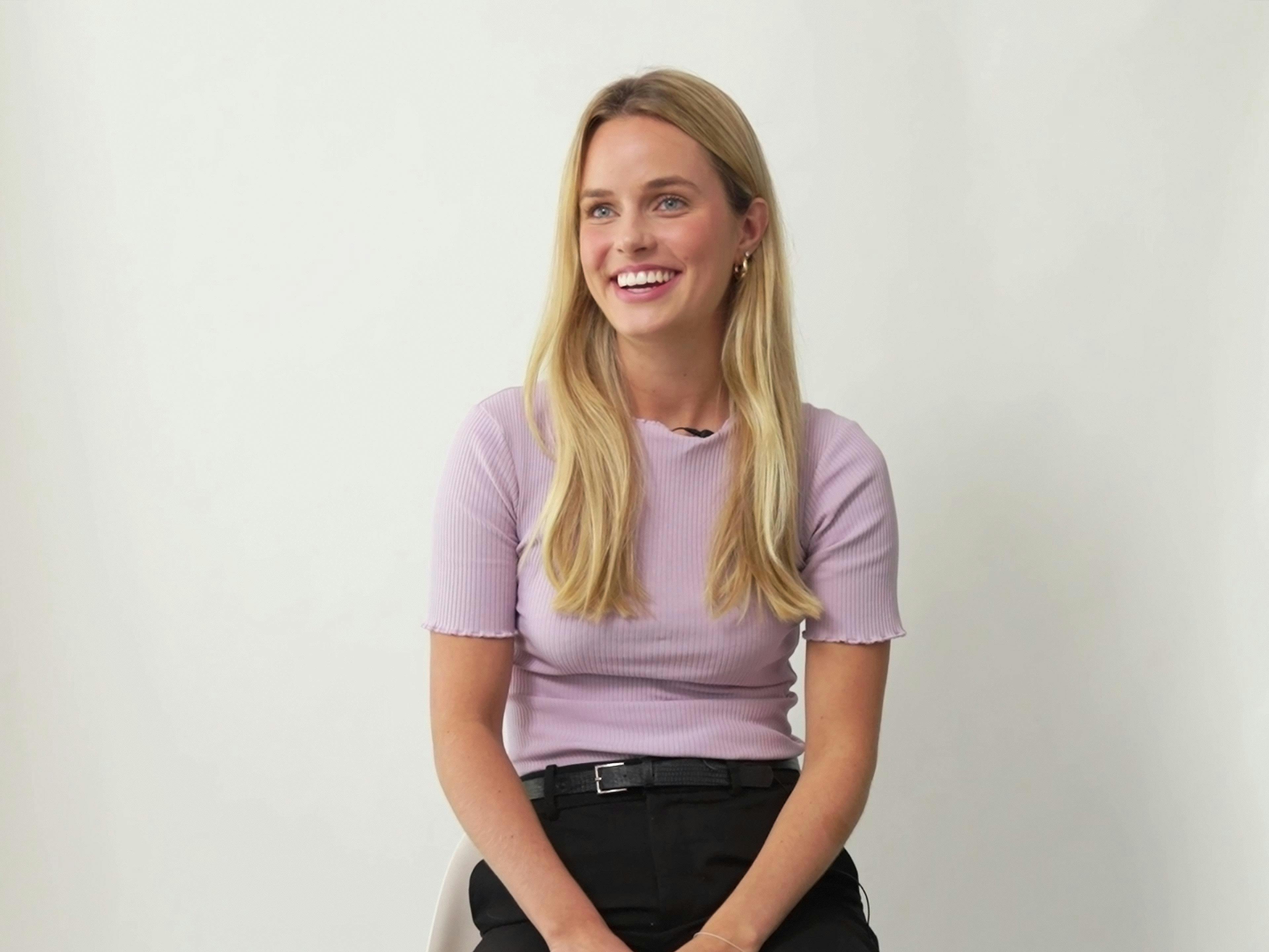 Porsche employee Anna sitting in front of the camera in an interview and smiling.