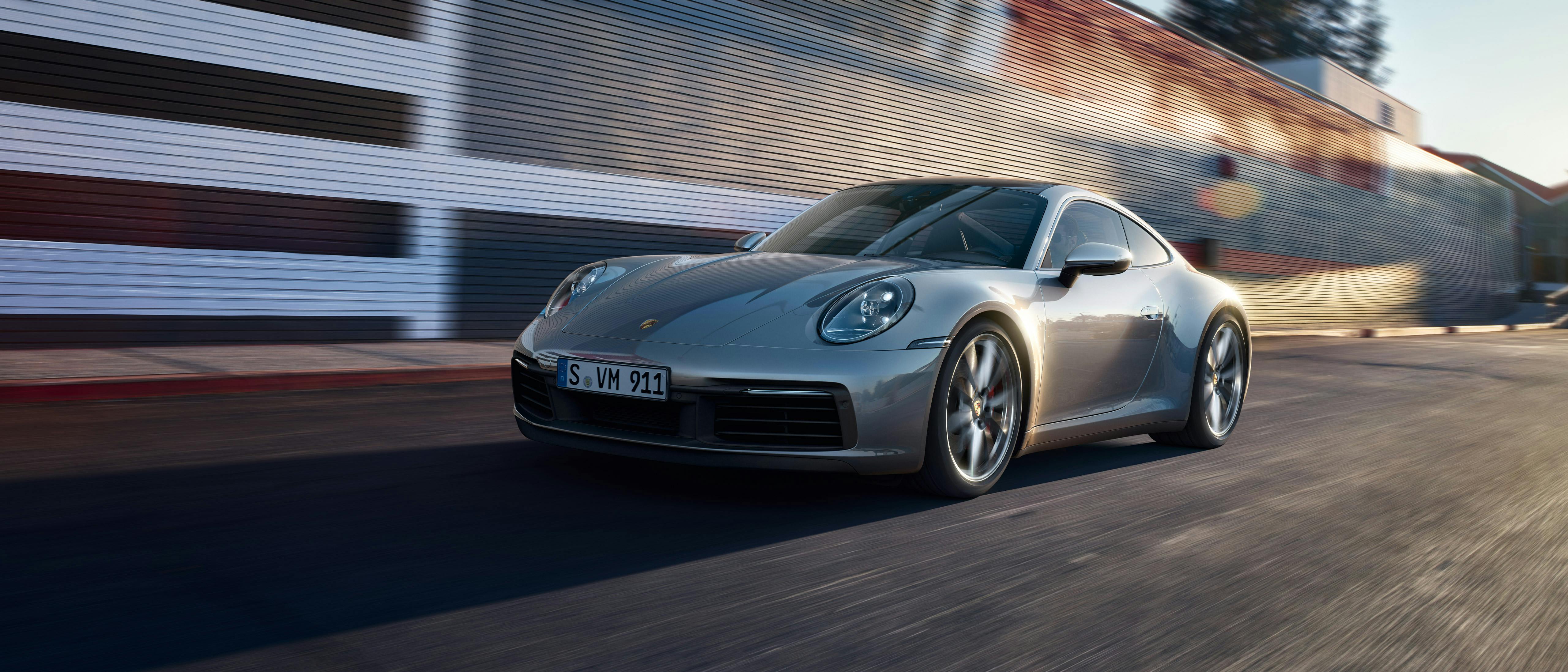 A silver Porsche 911 drives along a road.