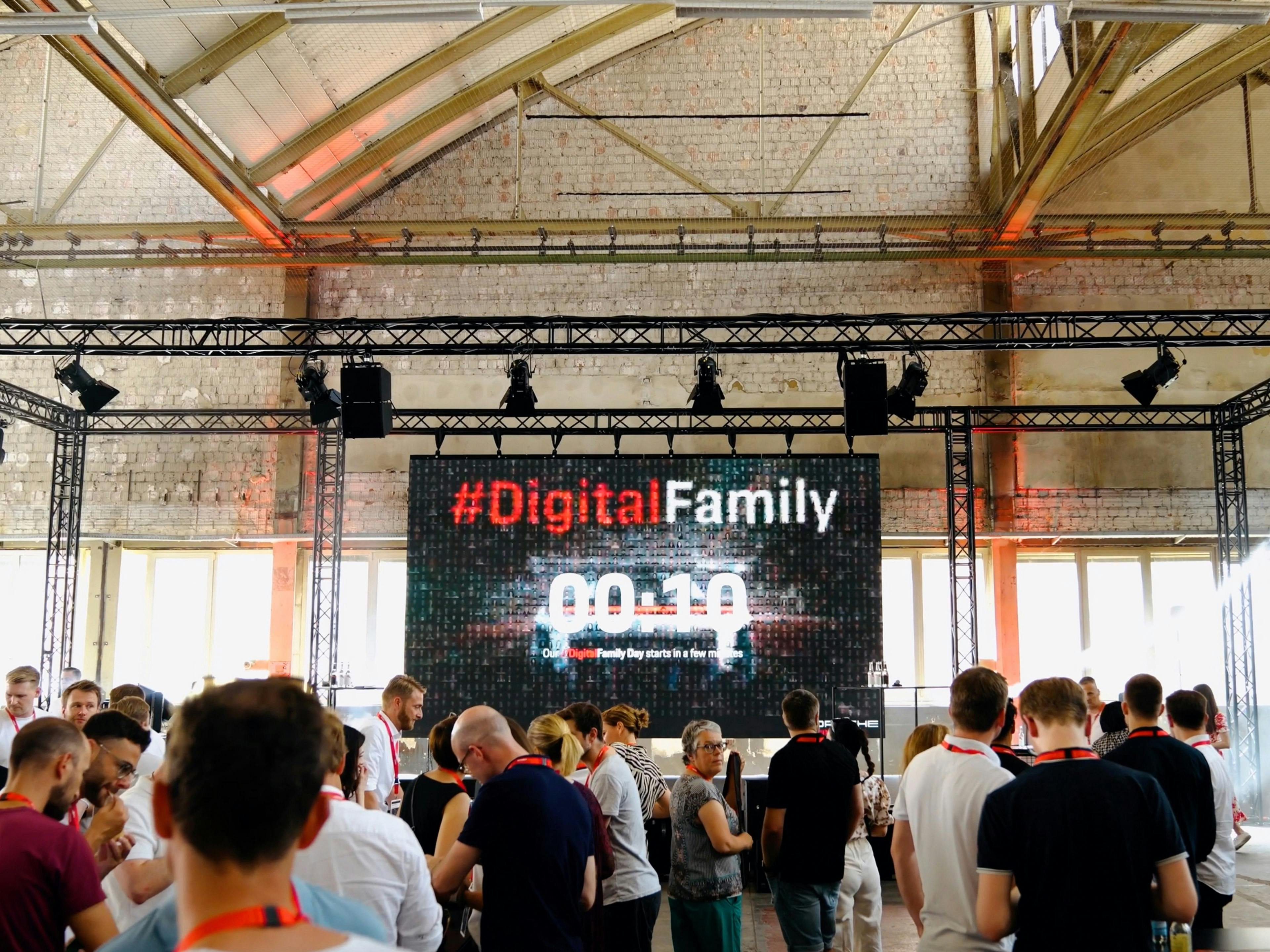 Viele Porsche Mitarbeiter warten in einer Industriehalle gespannt auf den Start des Digital Family Days.