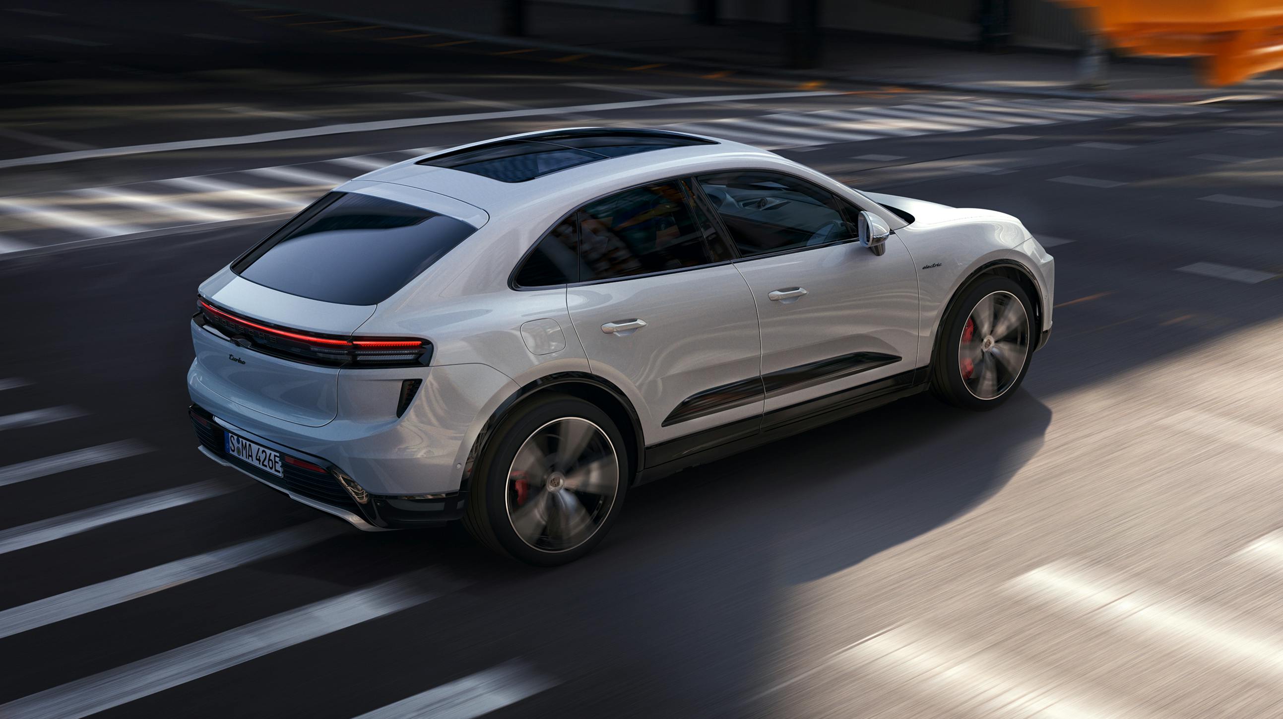 Porsche Macan Turbo in Ice Grey Metallic driving through a crossroads. Side view.