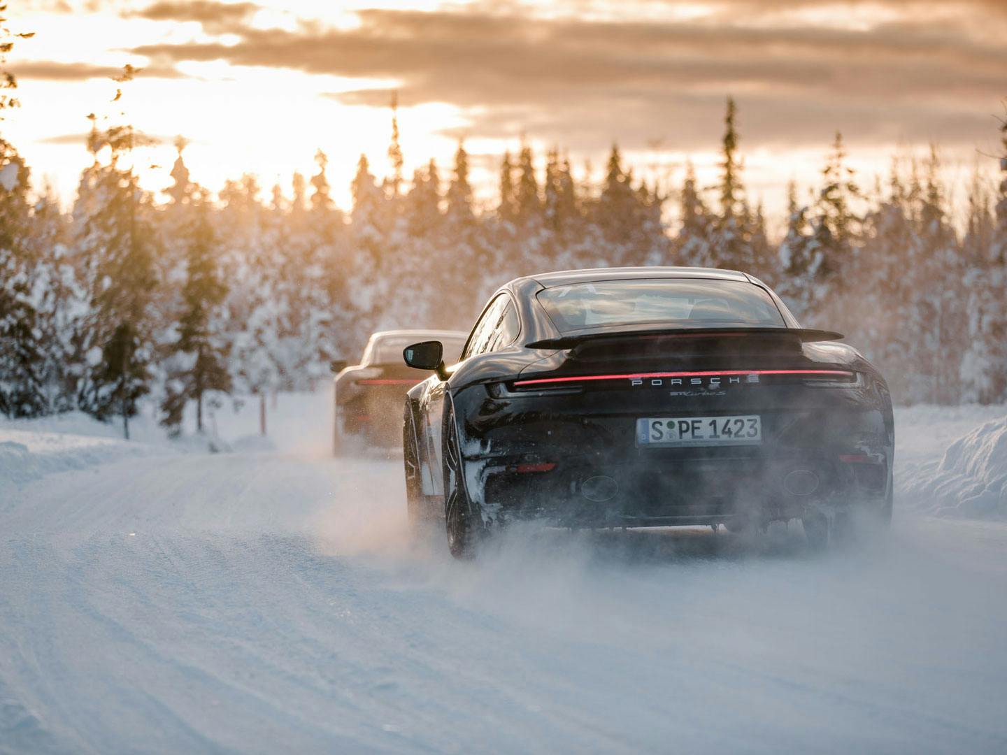 En svart Porsche kör genom ett snölandsskap.