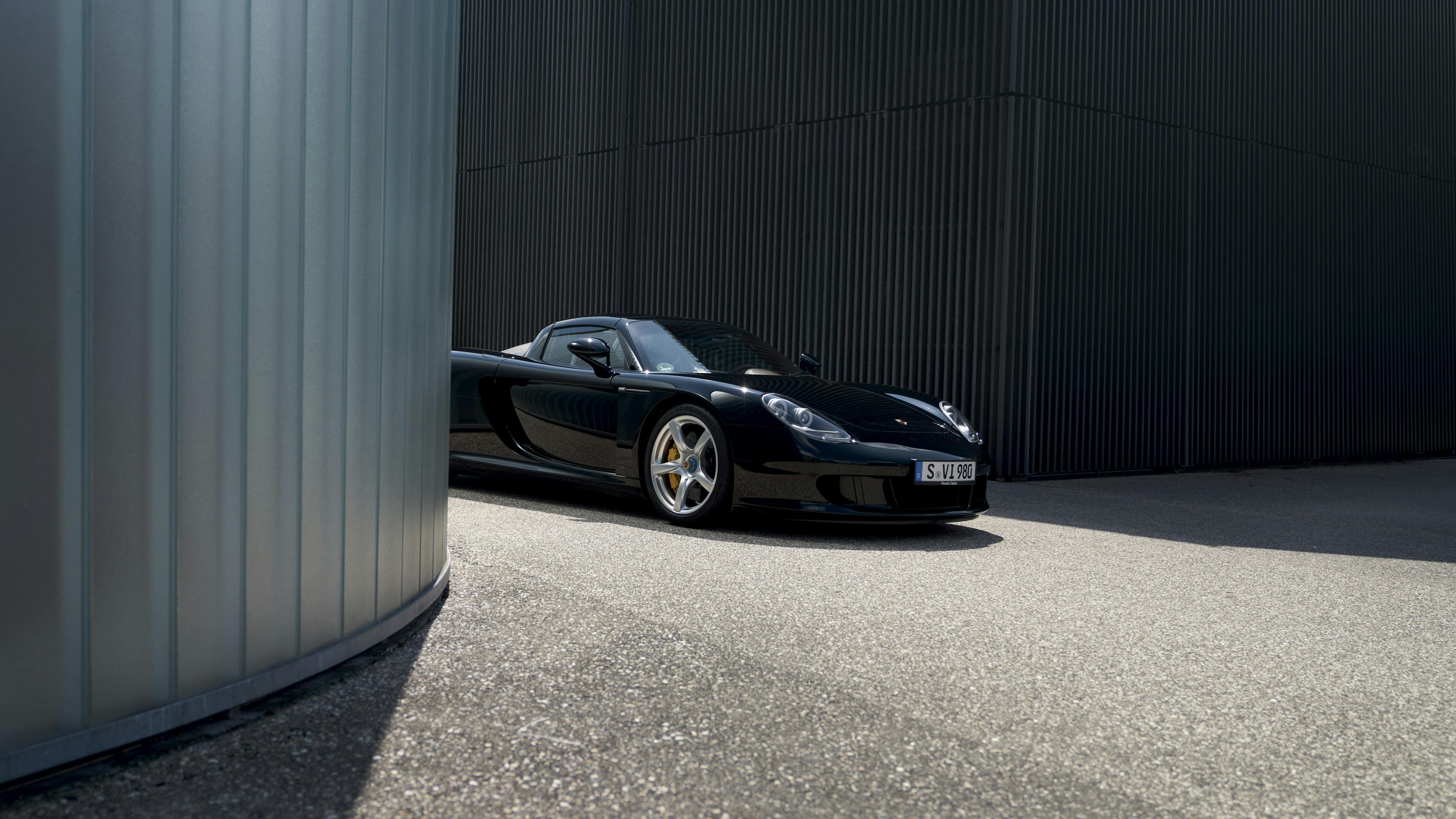 Front of a black Carrera GT driving round a bend alongside a building
