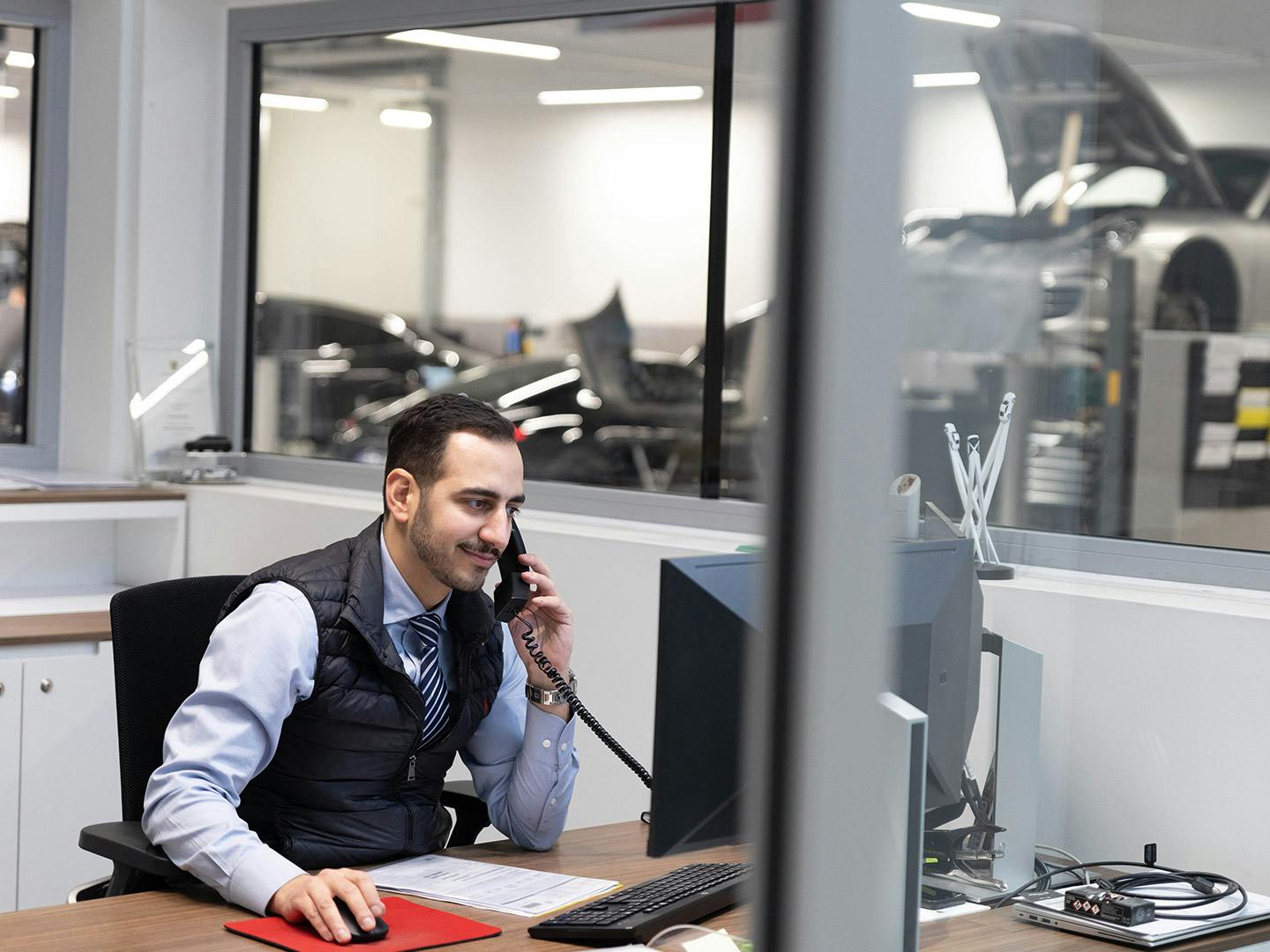 Un employé de Porsche, assis derrière un bureau, parle au téléphone tout en travaillant sur un ordinateur devant lui.