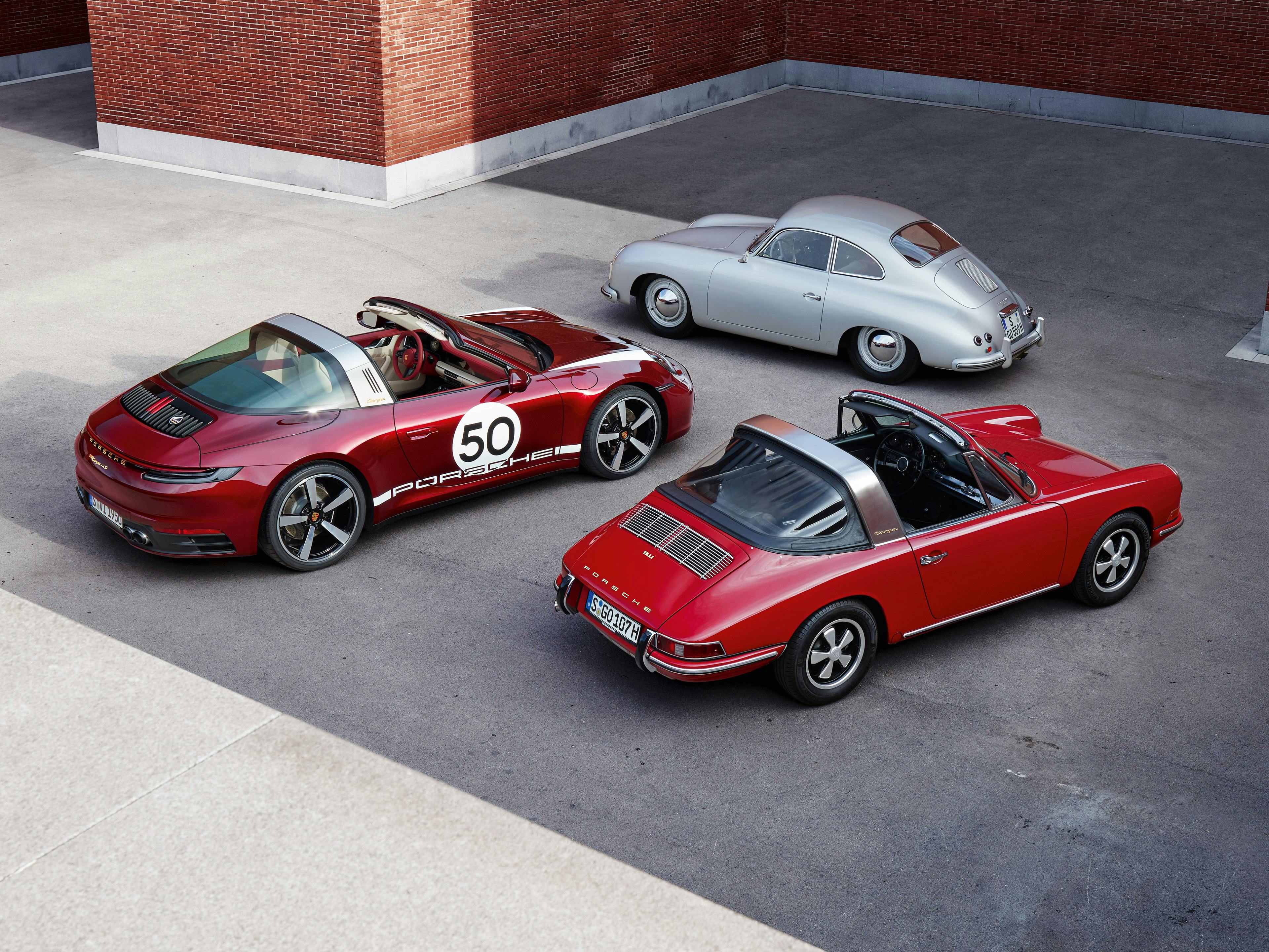 Porsche 356 grigia, 911 992 Targa 4S rossa e 911 Targa Classic rossa parcheggiate vicino a un muro di mattoni