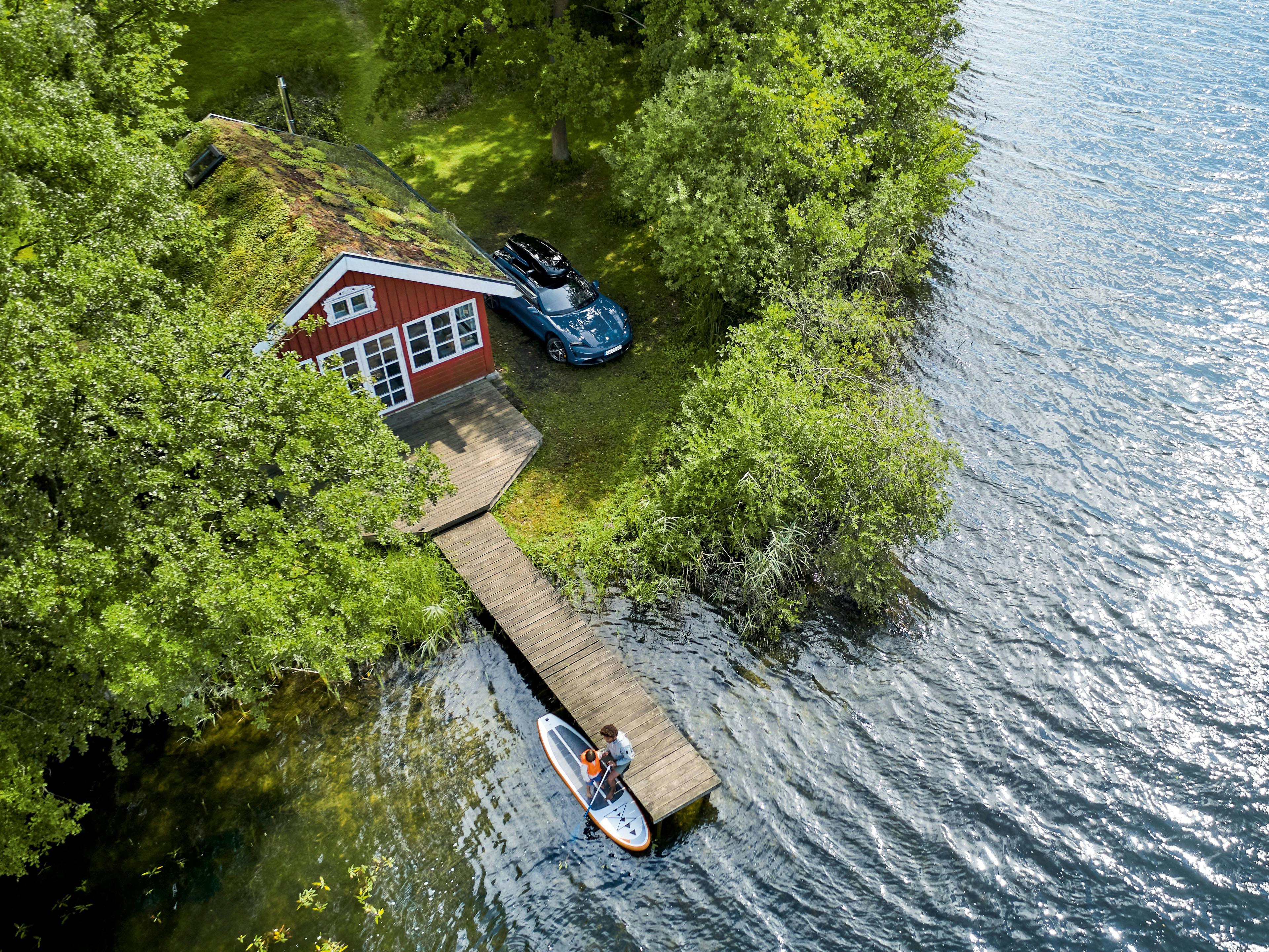 Idyllisches Ferienhaus mit Steg an einem See mit parkendem Taycan Turbo S Cross neben dem Haus.