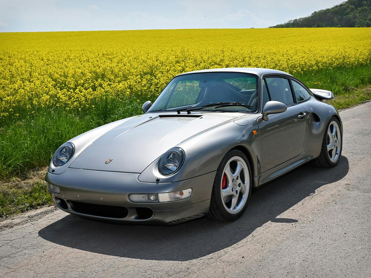 A 911 Turbo (993) painted in Liquid Metal Silver in front of a yellow flower field.