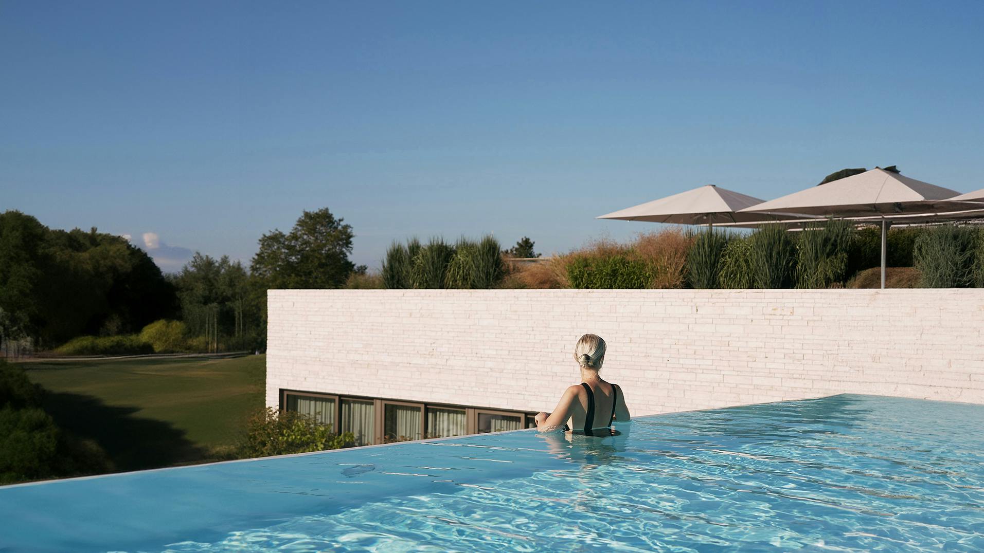 Eine Frau steht am Rand im Pool des Öschberghof und genießt die Aussicht.