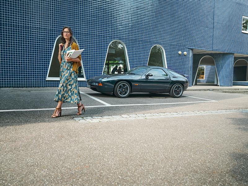 Blue Porsche 928 in front of a blue tiled building.