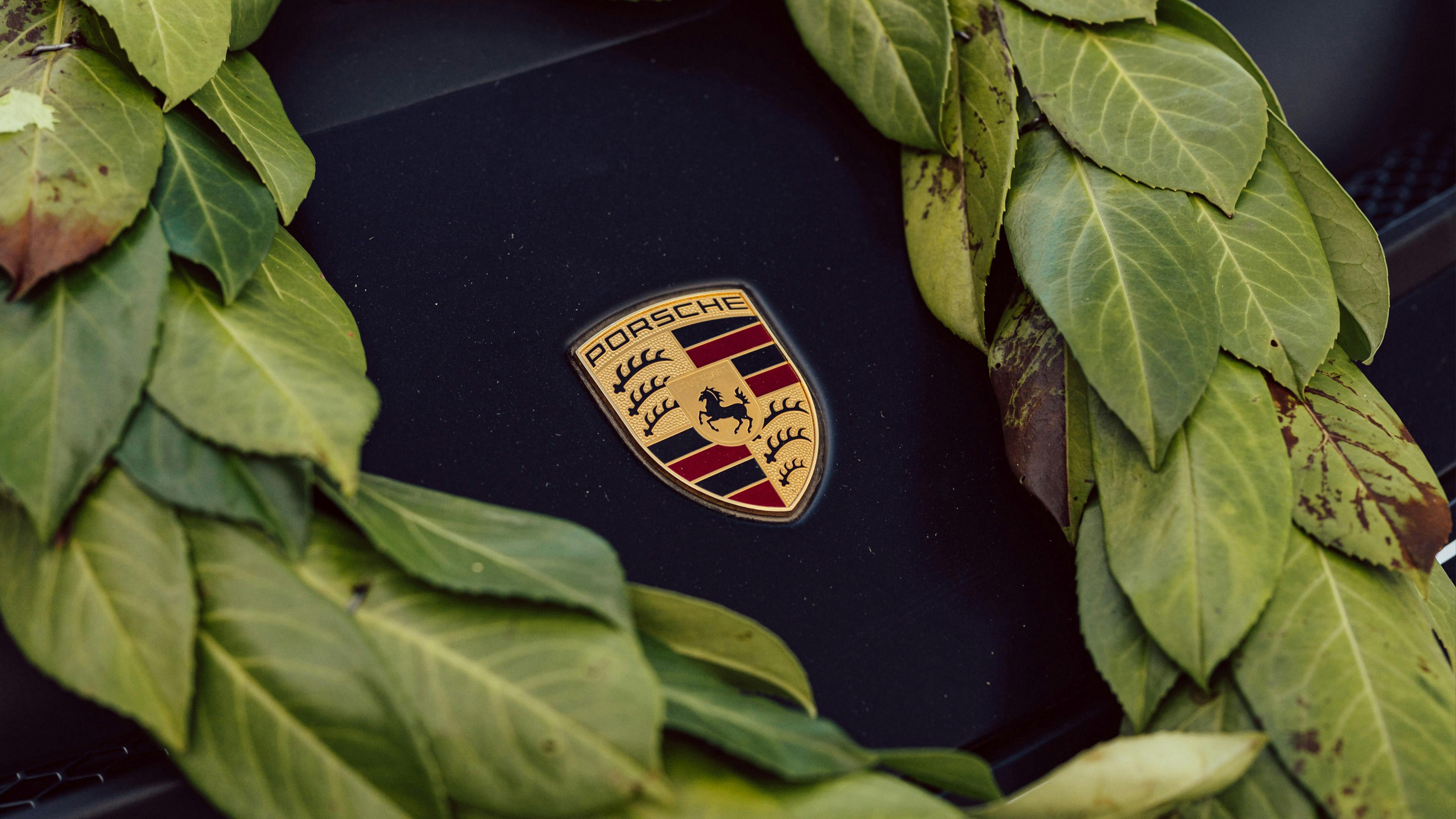 A close-up of a Porsche crest badge on a dark bonnet, framed by a laurel wreath symbolising motorsport victory.