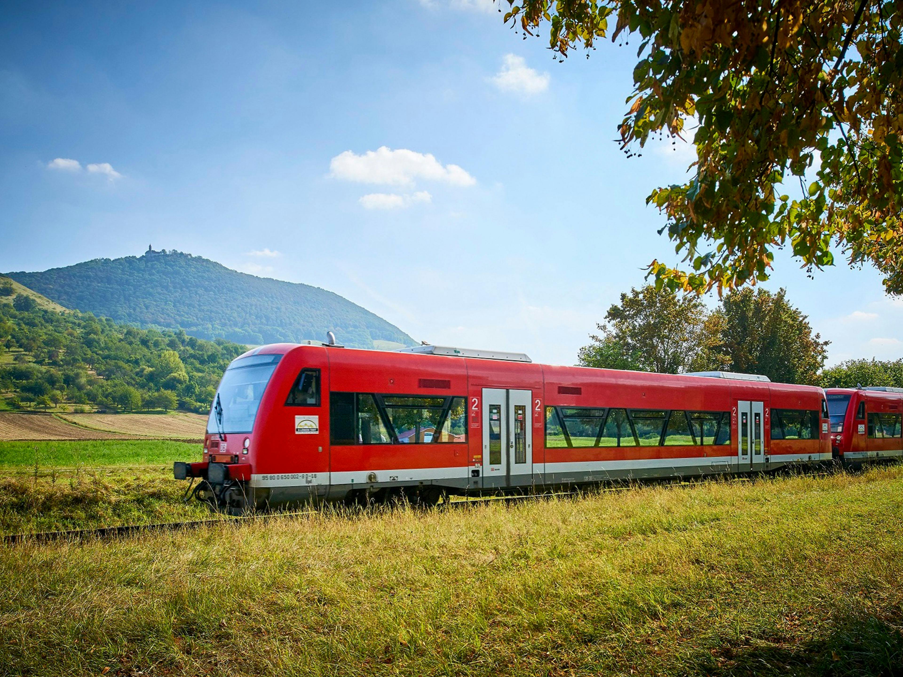 Rote Zug-Waggons der Deutschen Bahn fahren durch eine grüne Landschaft.