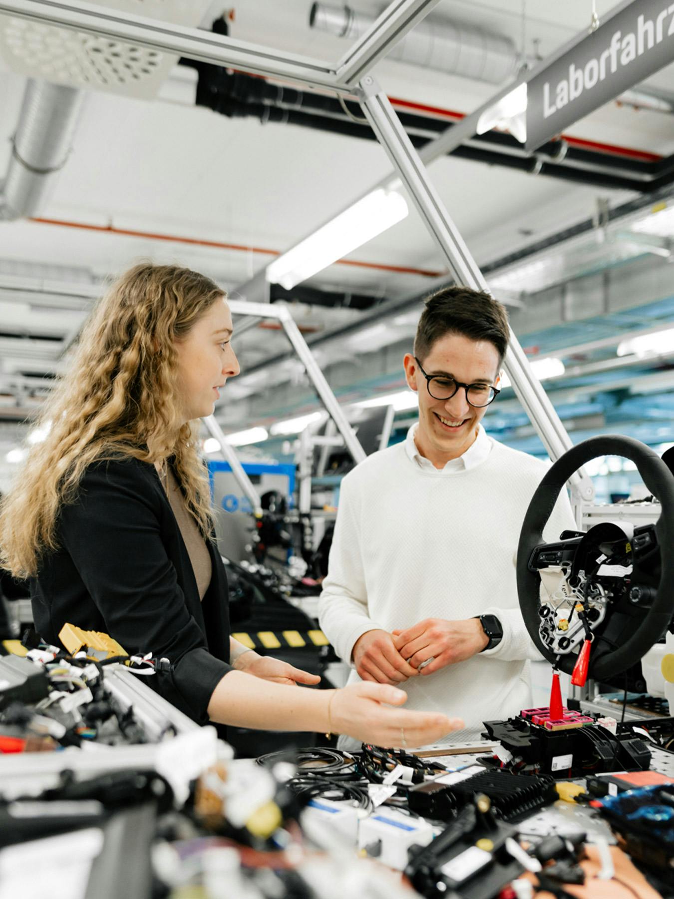 Eine Auszubildende und ein dualer Student stehen an einem Porsche Prüfstand