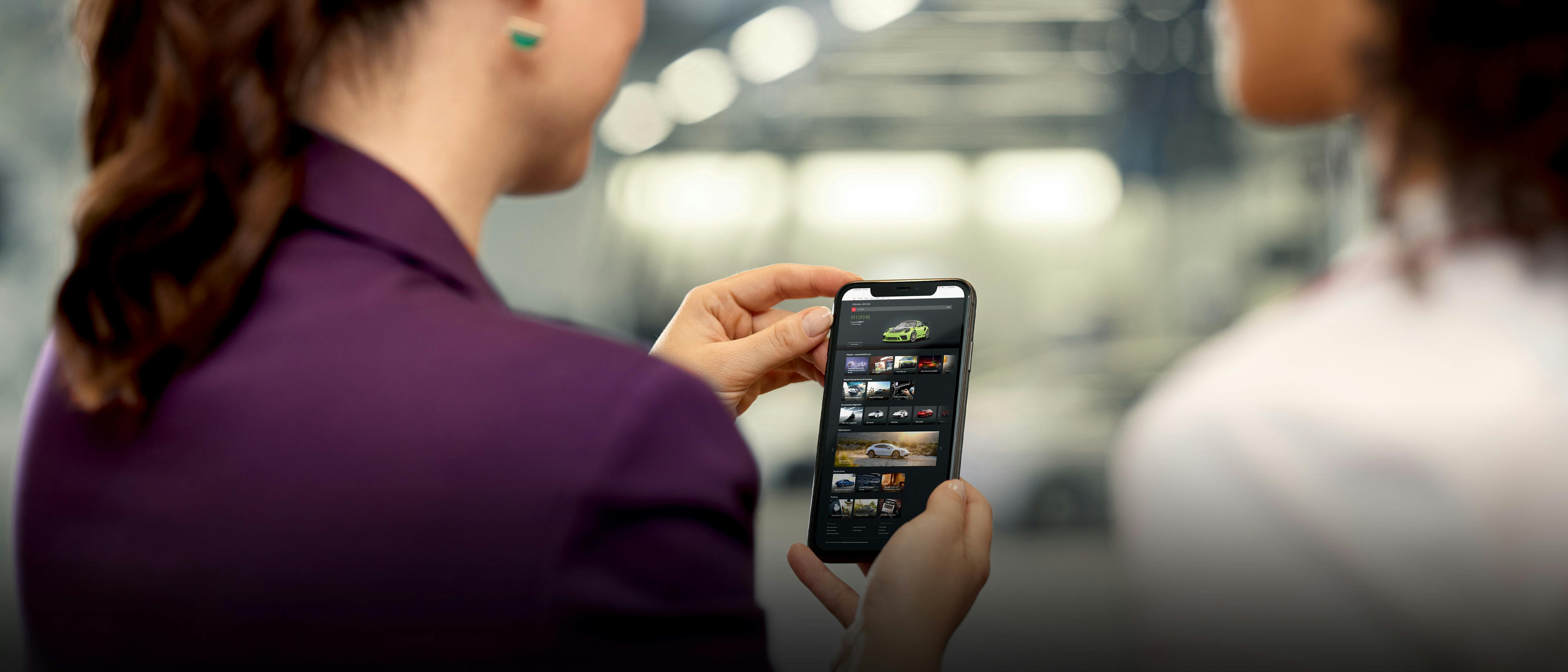 Deux femmes de dos, regardant par-dessus leur épaule un smartphone avec l'application My Porsche à l'écran.