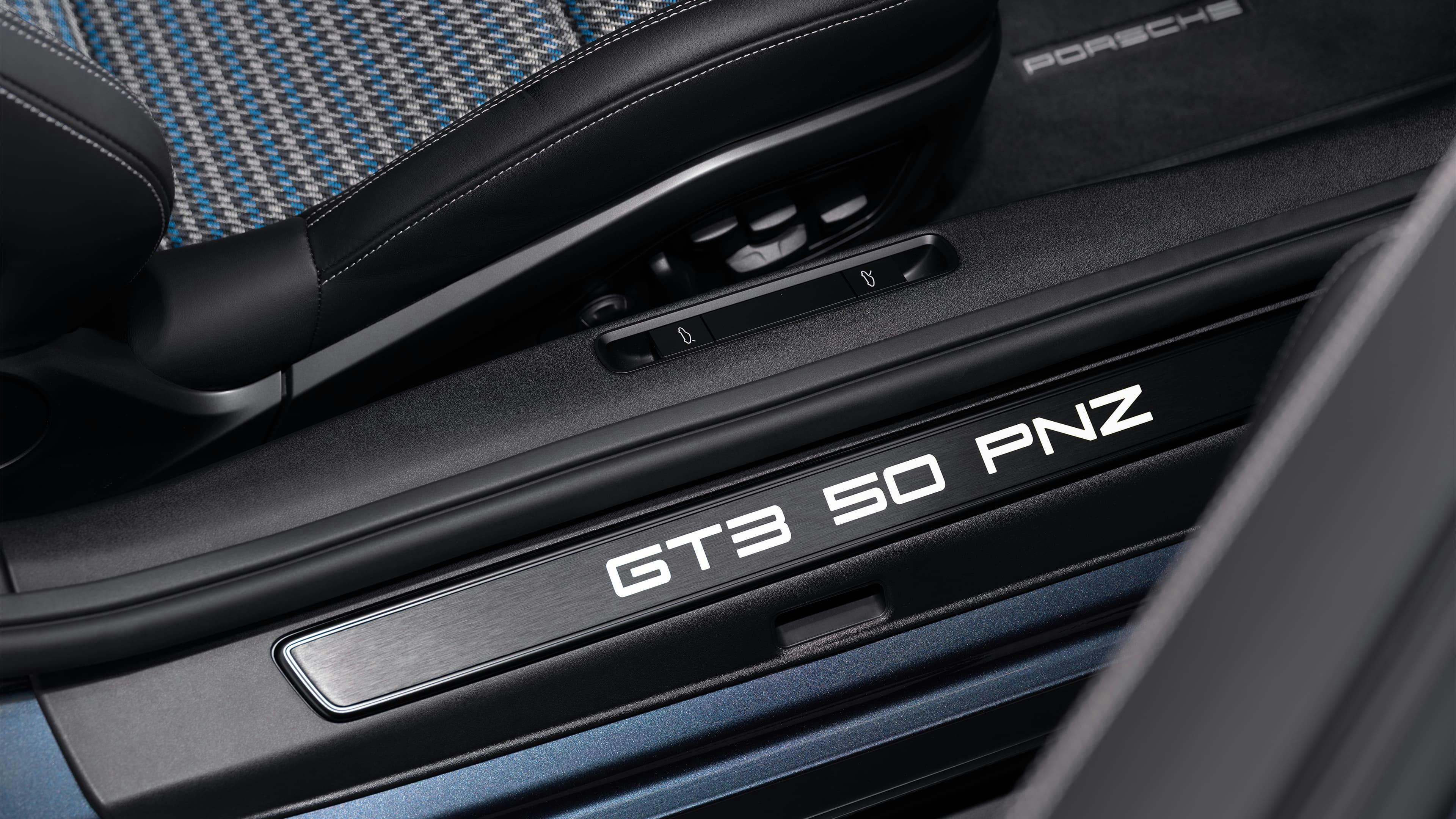 Close-up of a car door sill plate illuminated with the text 'GT3 50 PNZ', beside a patterned sports seat.