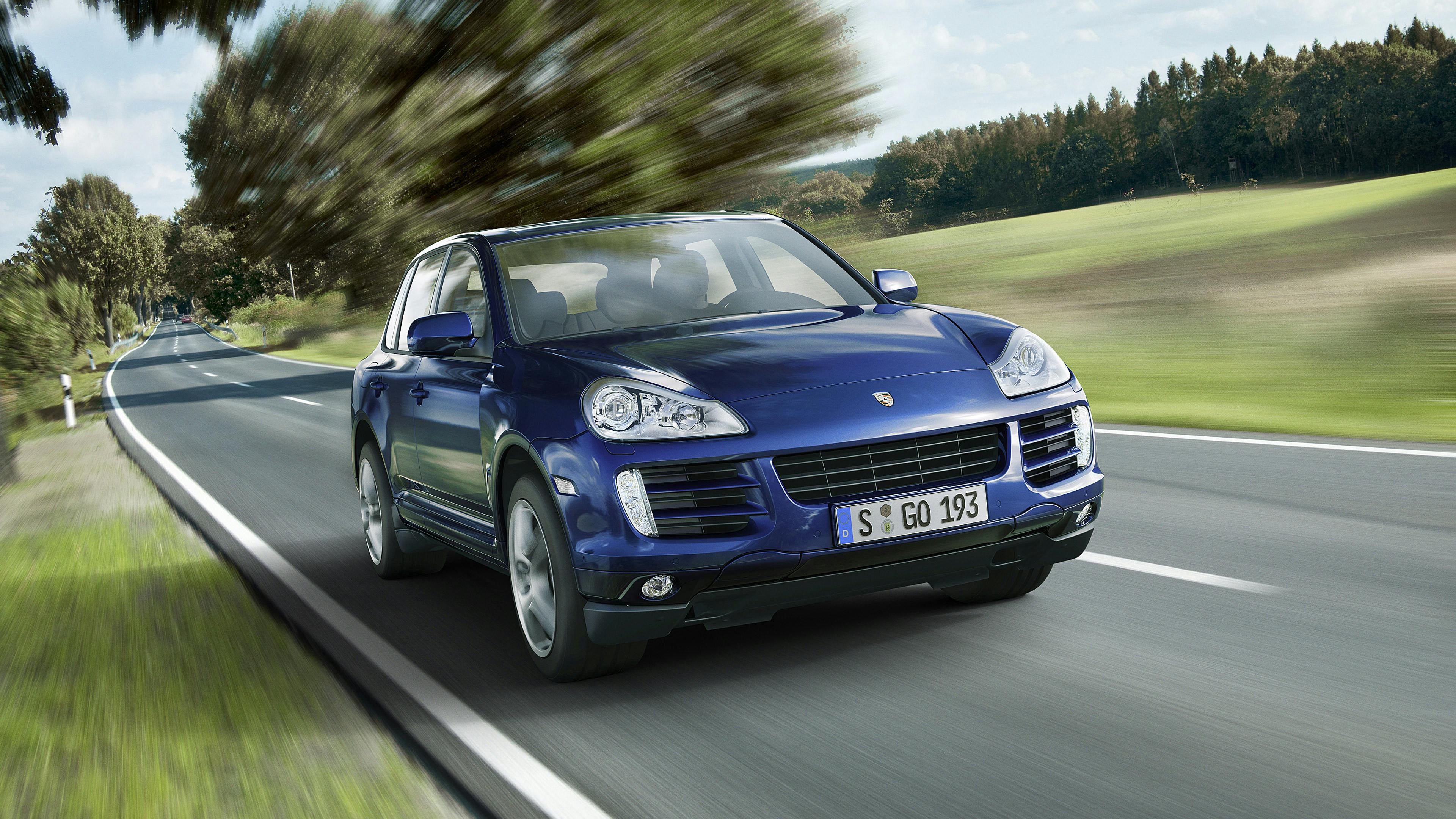 Cayenne Diesel de color Azul (2009-10) desplazándose por carreteras secundarias, con árboles y prados.