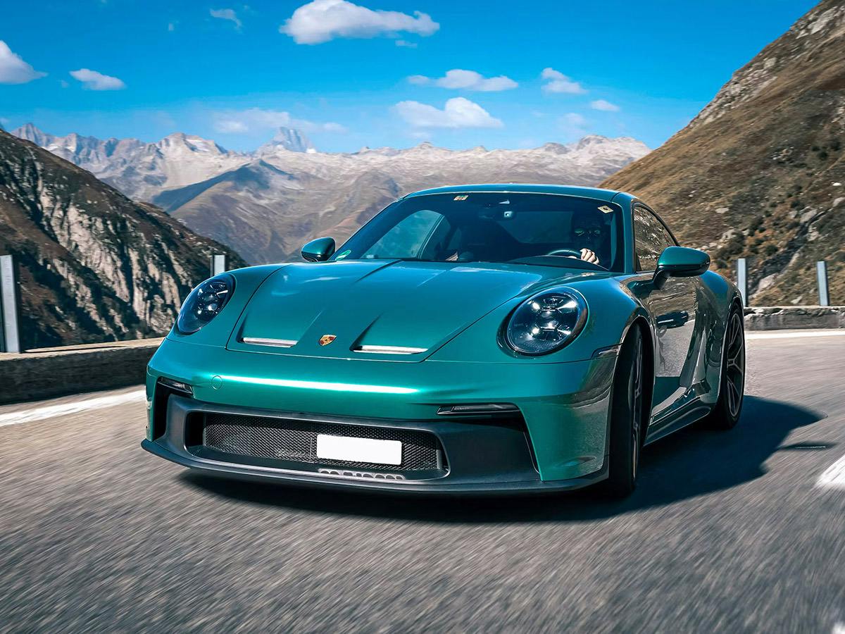 A 911 GT3 Touring in individual colour Racing Green Metallic on a road in the mountains.