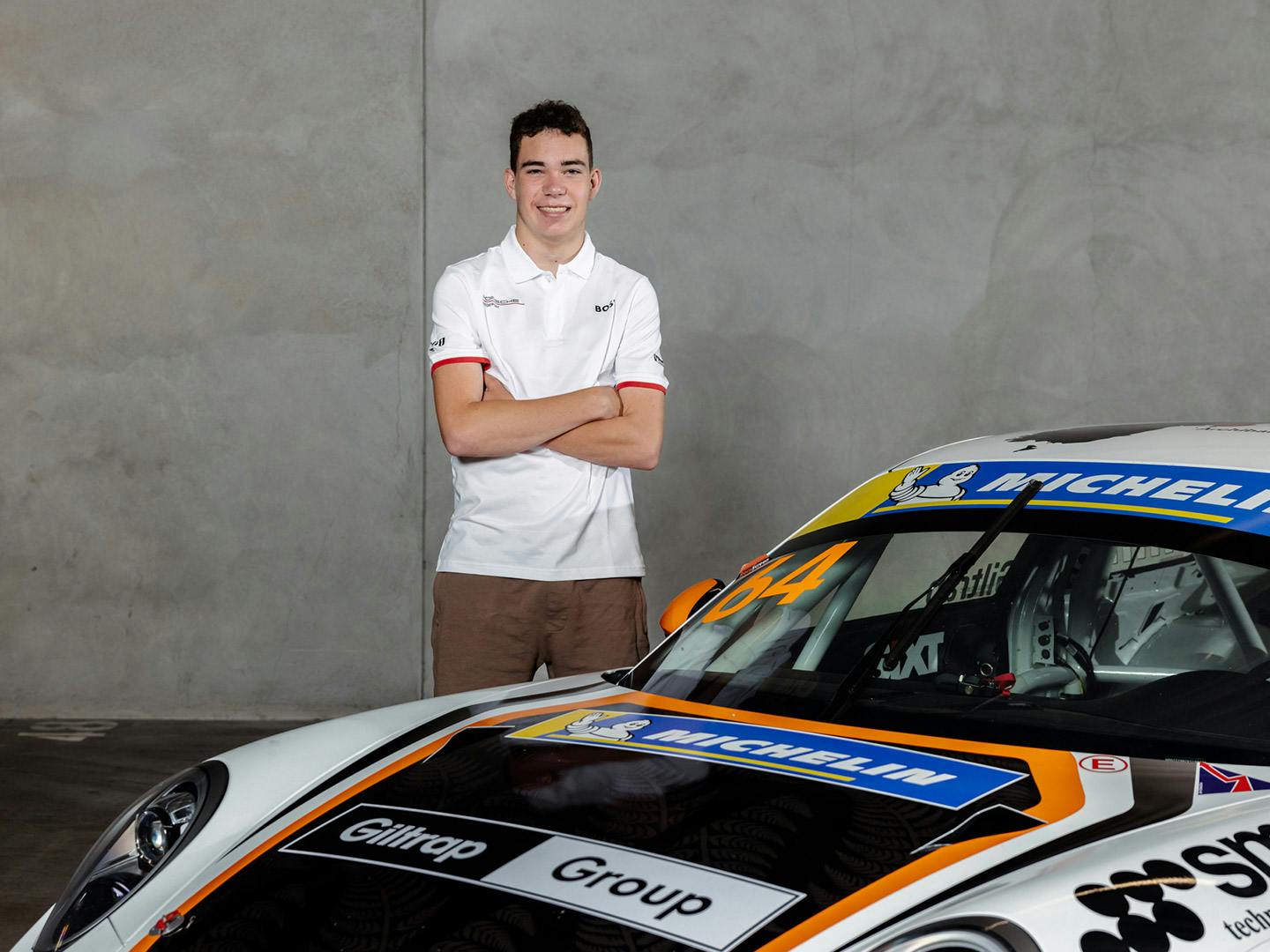 Tom Bewley stands next to a green Porsche with his arms folded, smiling.