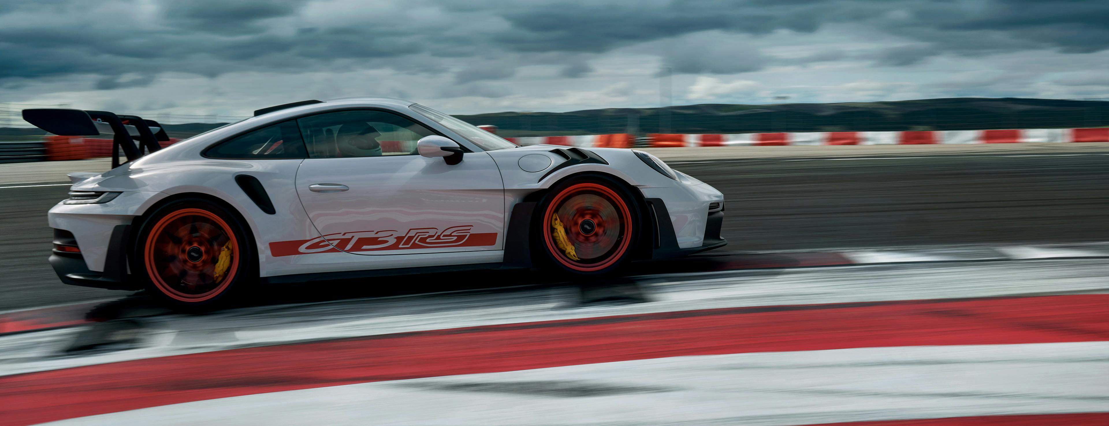 White Porsche 911 GT3 with red highlights, driving on racetrack.