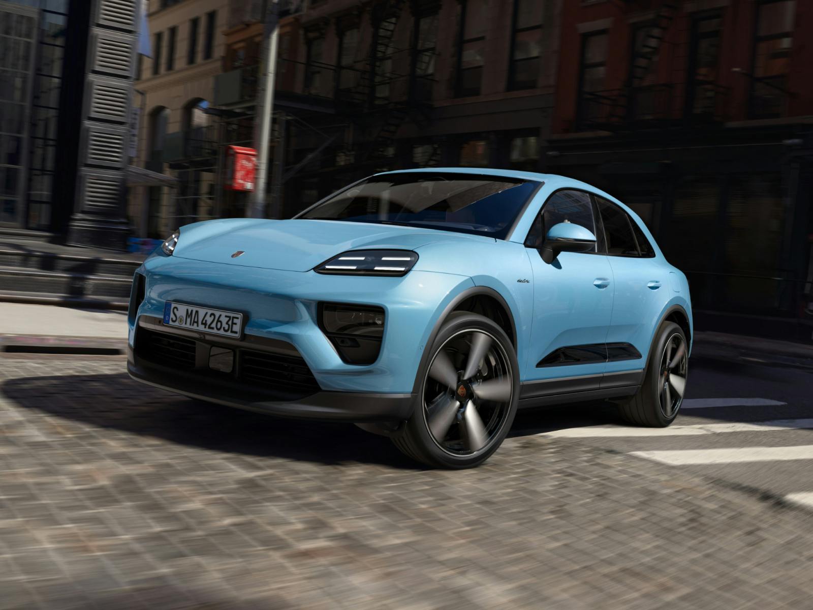 Porsche Macan in Frozen Blue Metallic driving through an intersection. Front view of the front and side.