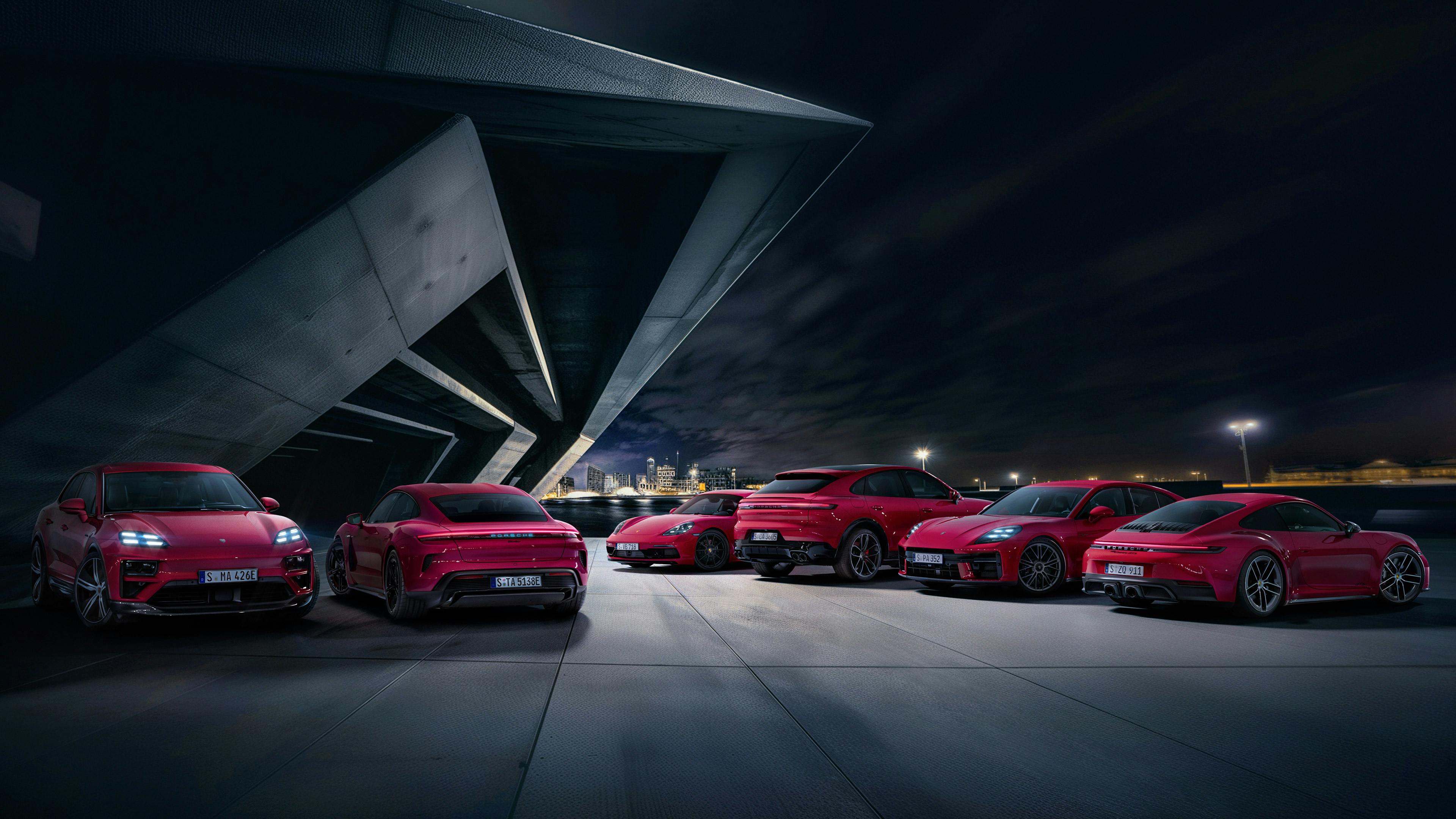 A full rage of Carmine Red Porsche models sits parked in front of a modern building at night.
