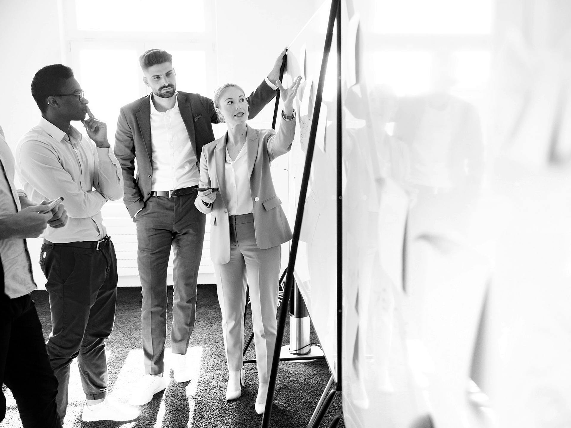 Black-and-white photo: several Porsche employees are standing and conducting a meeting at a presentation wall.