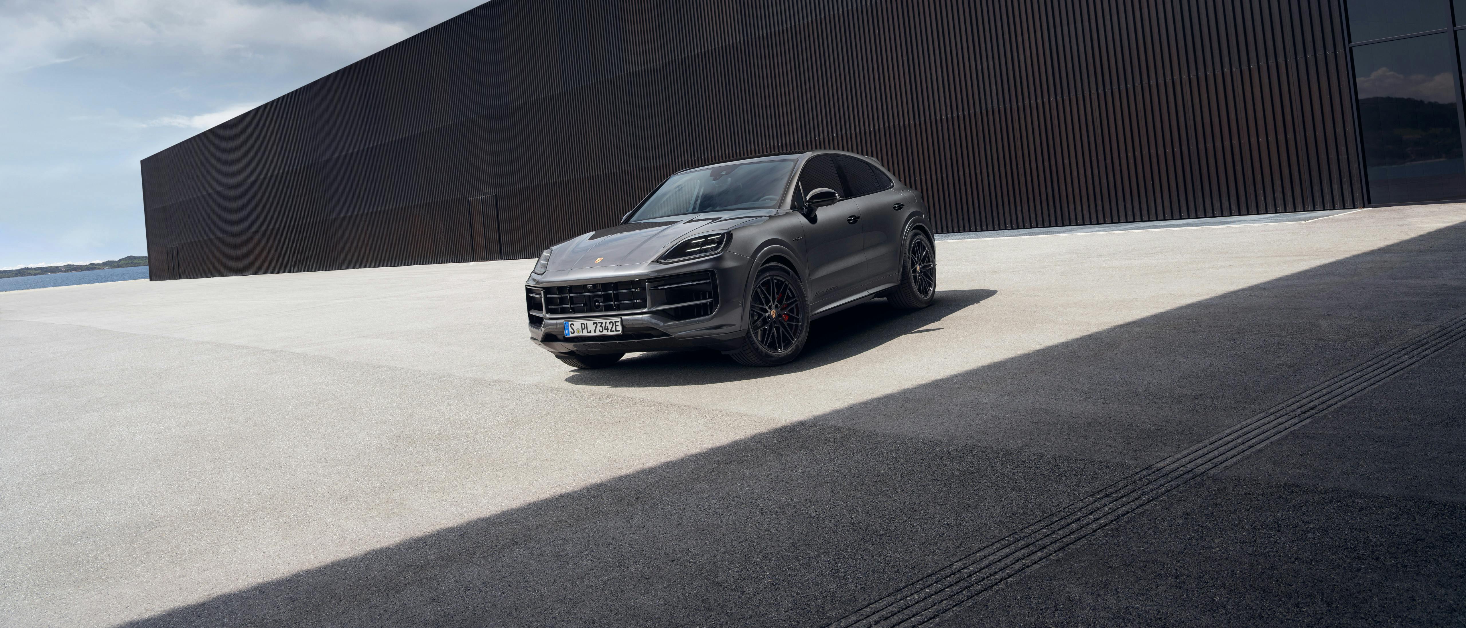 The Cayenne S E-Hybrid Coupé Black Edition parked outside a modern building that is made up of dark textured material and also glass.