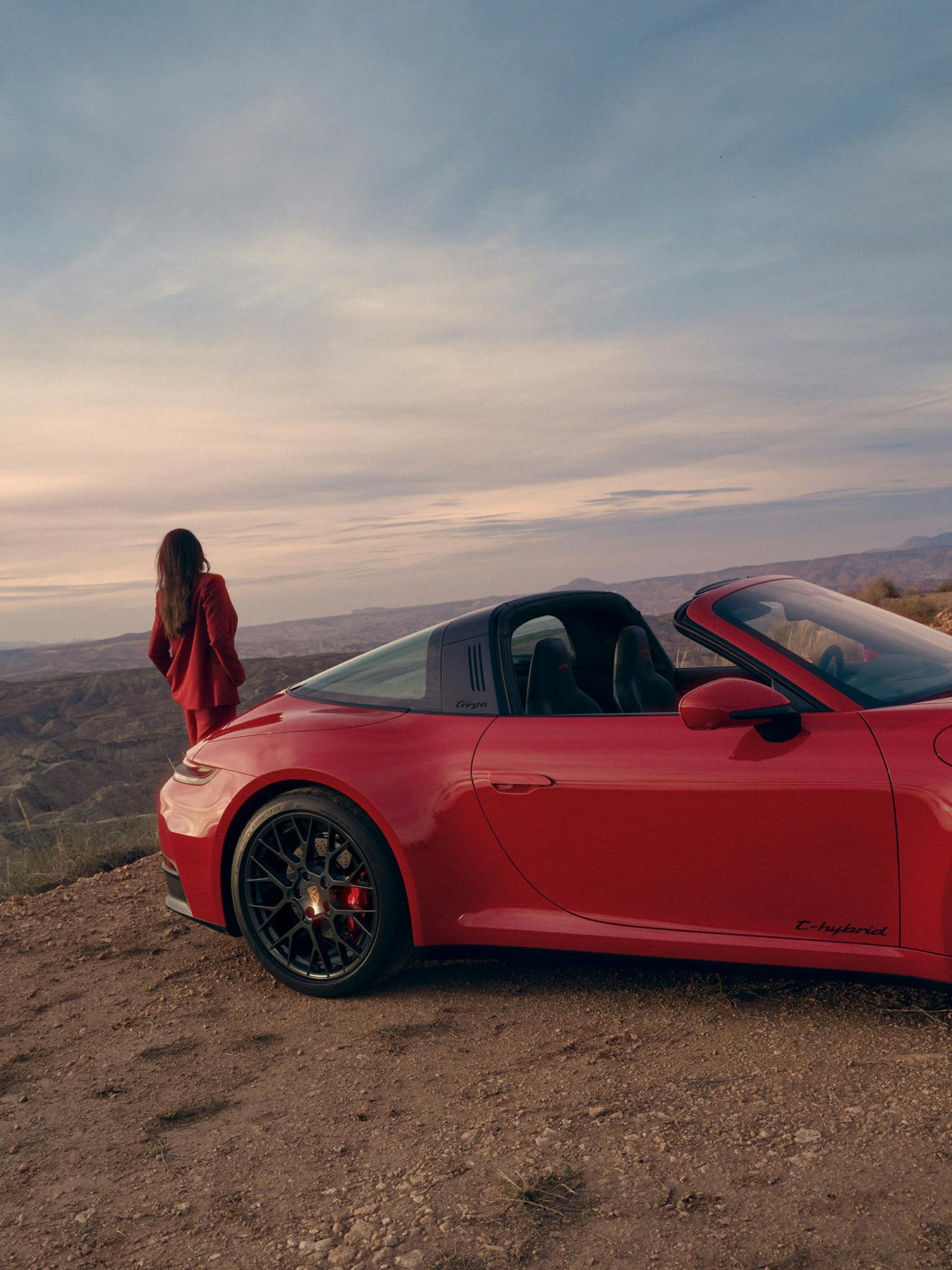 Roter Porsche 911 Targa steht auf einer Anhöhe in einer weiten Landschaft, während eine Person daneben steht und in die Ferne blickt