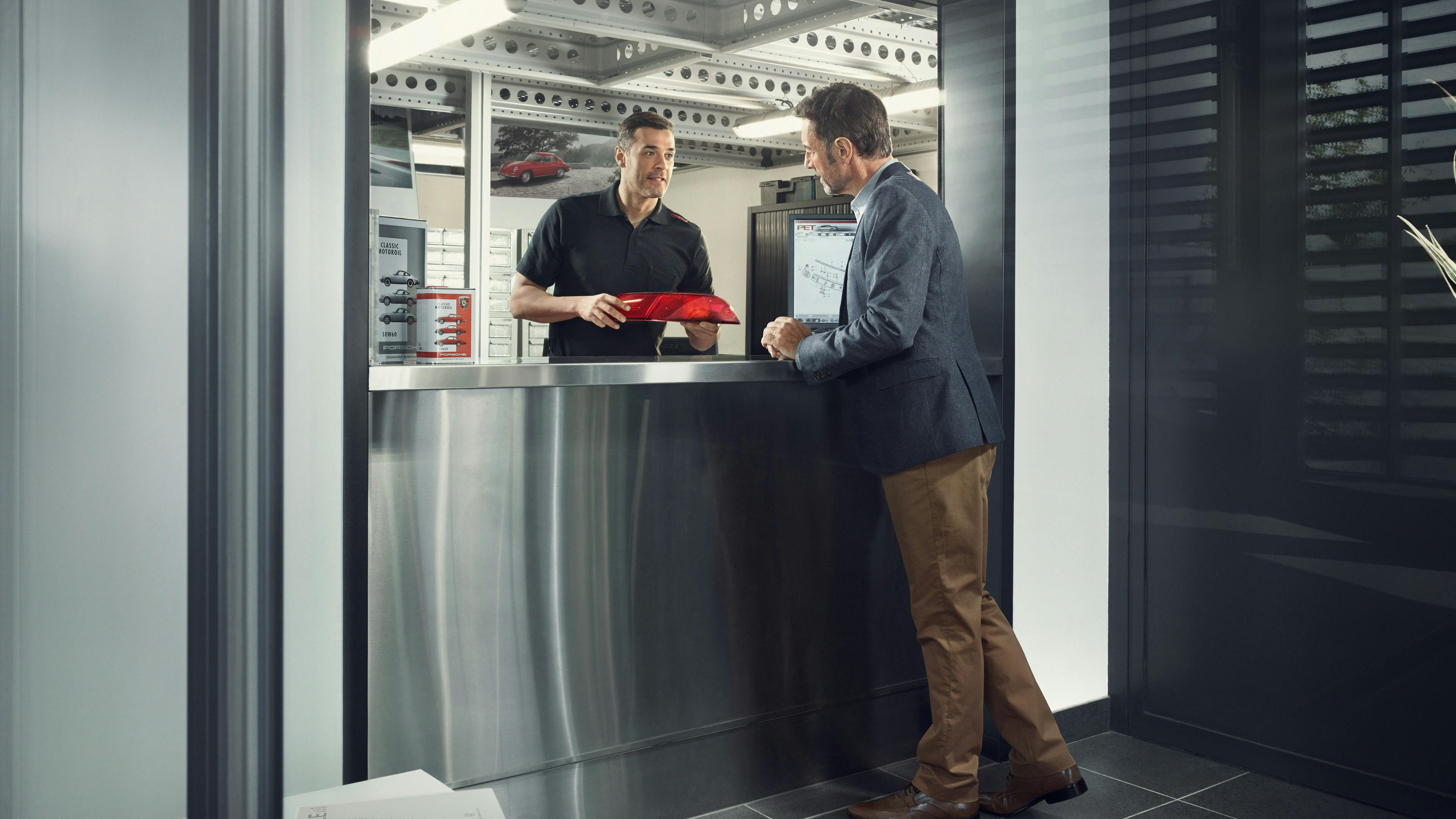 Porsche Servicepartner im Ersatzteil-Sortiment berät einen Classic-Enthusiasten.