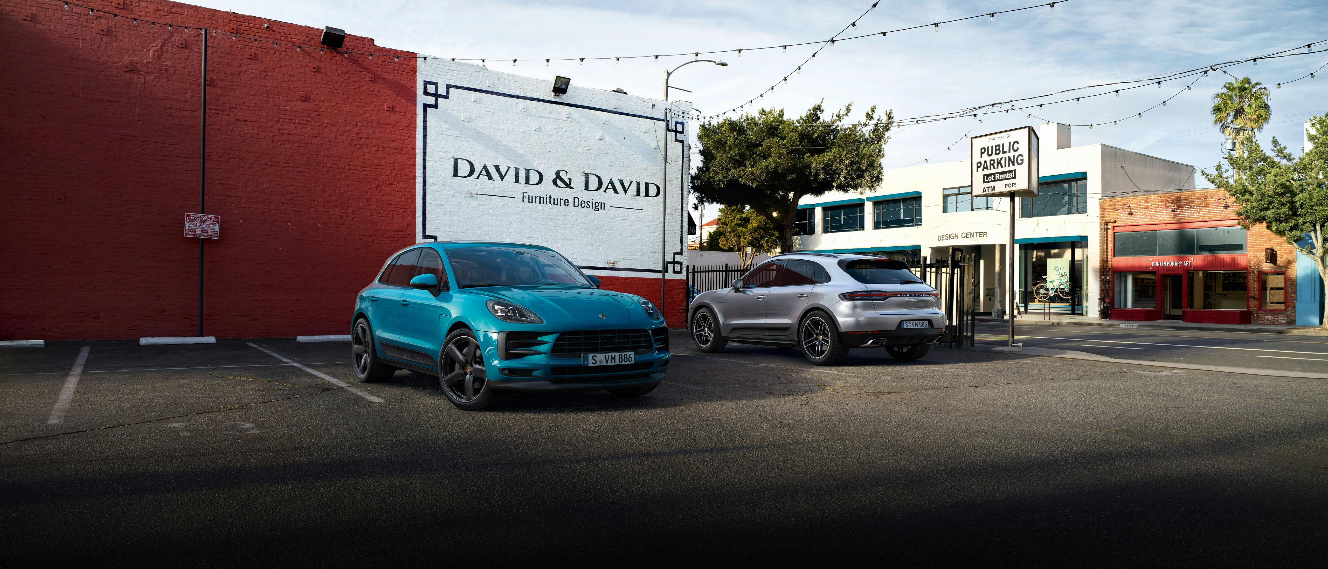 Deux Porsche Macan garées sur un parking à côté d'un mur rouge.