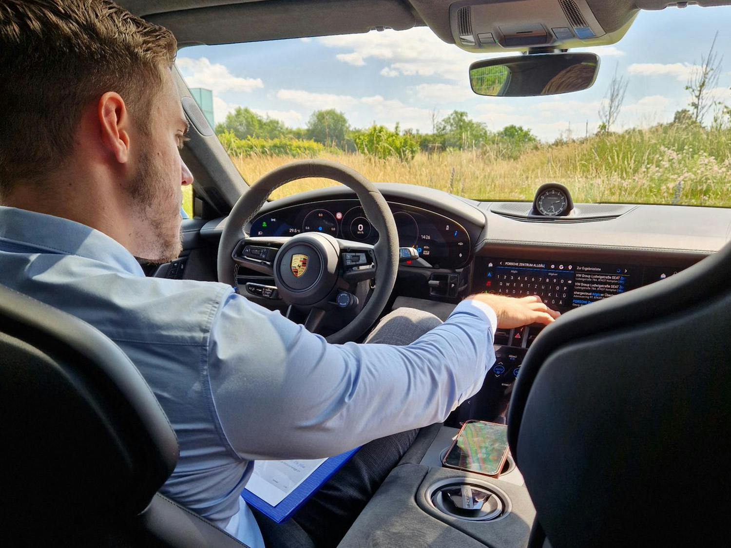 Porsche Innenraum mit Fahrer und schwarzem Armaturenbrett und Lenkrad, verschwommene Landschaft im Hintergrund.