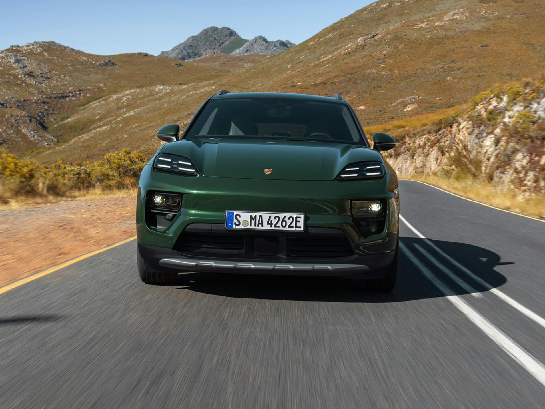 Front view of a Porsche Macan 4S driving on a road through a mountain landscape.