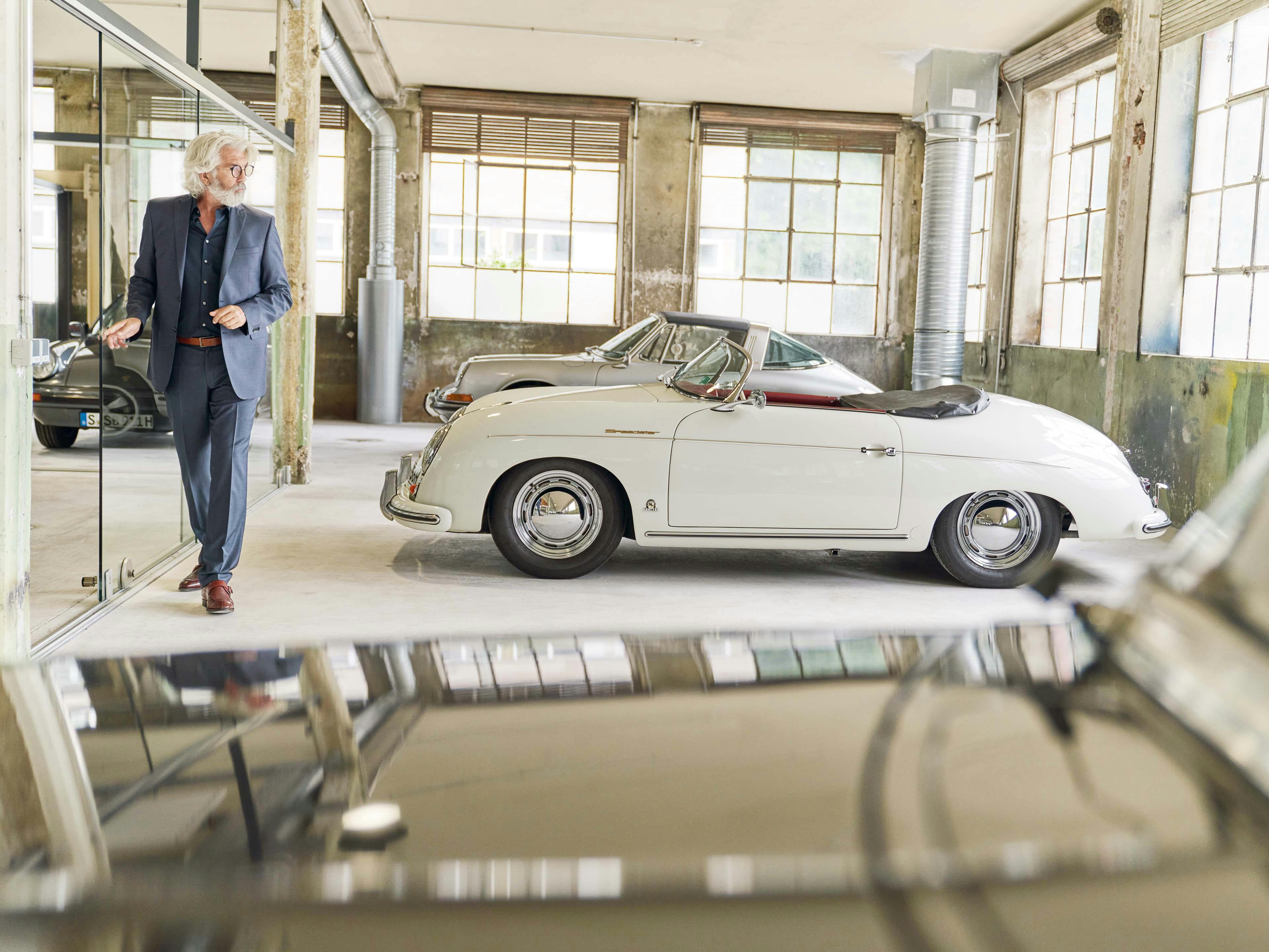 Een man staat naast een Porsche 356 in een loods.