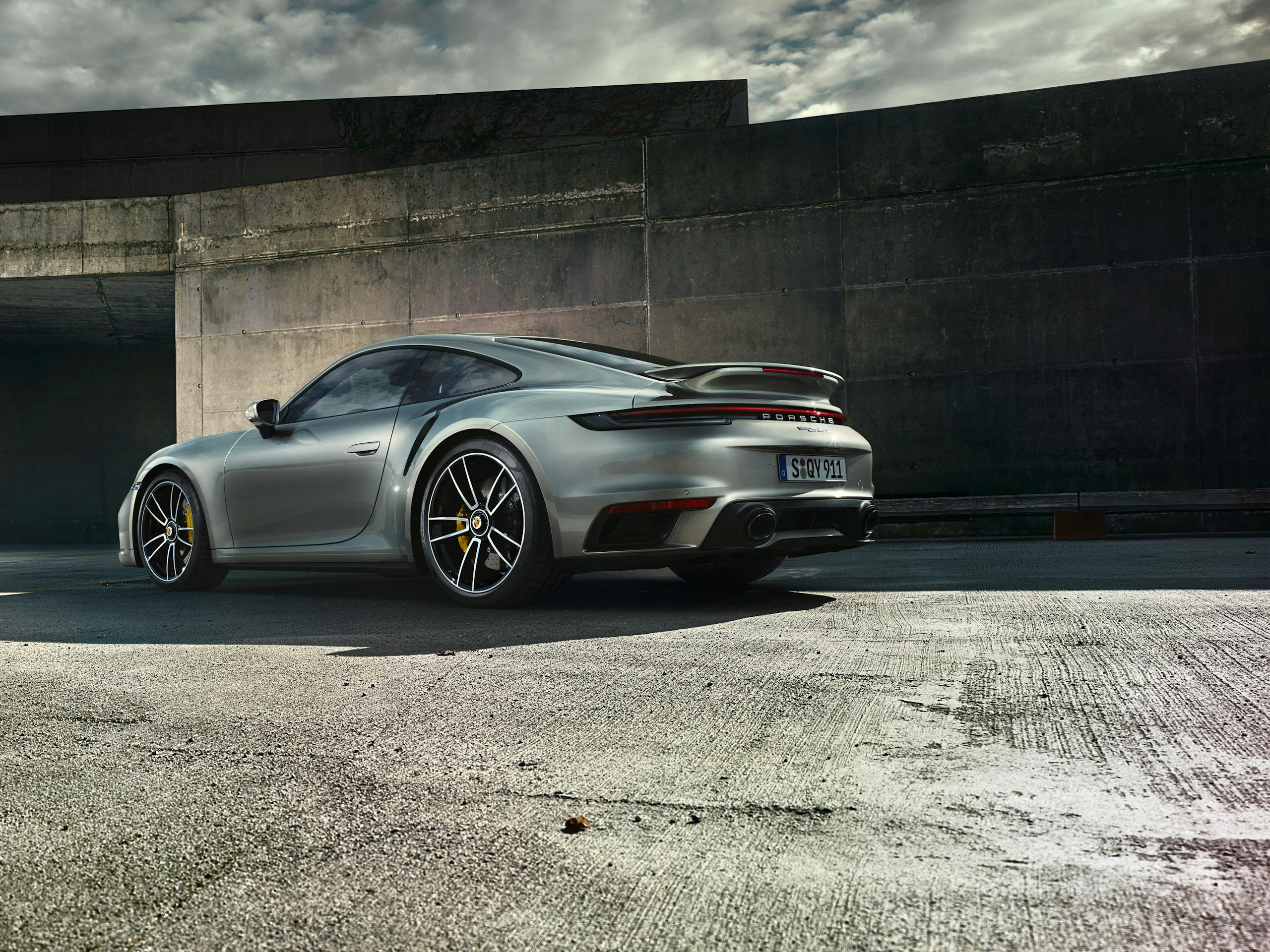 Side shot of a gray 911 Turbo S Coupe standing on an industrial site with older halls