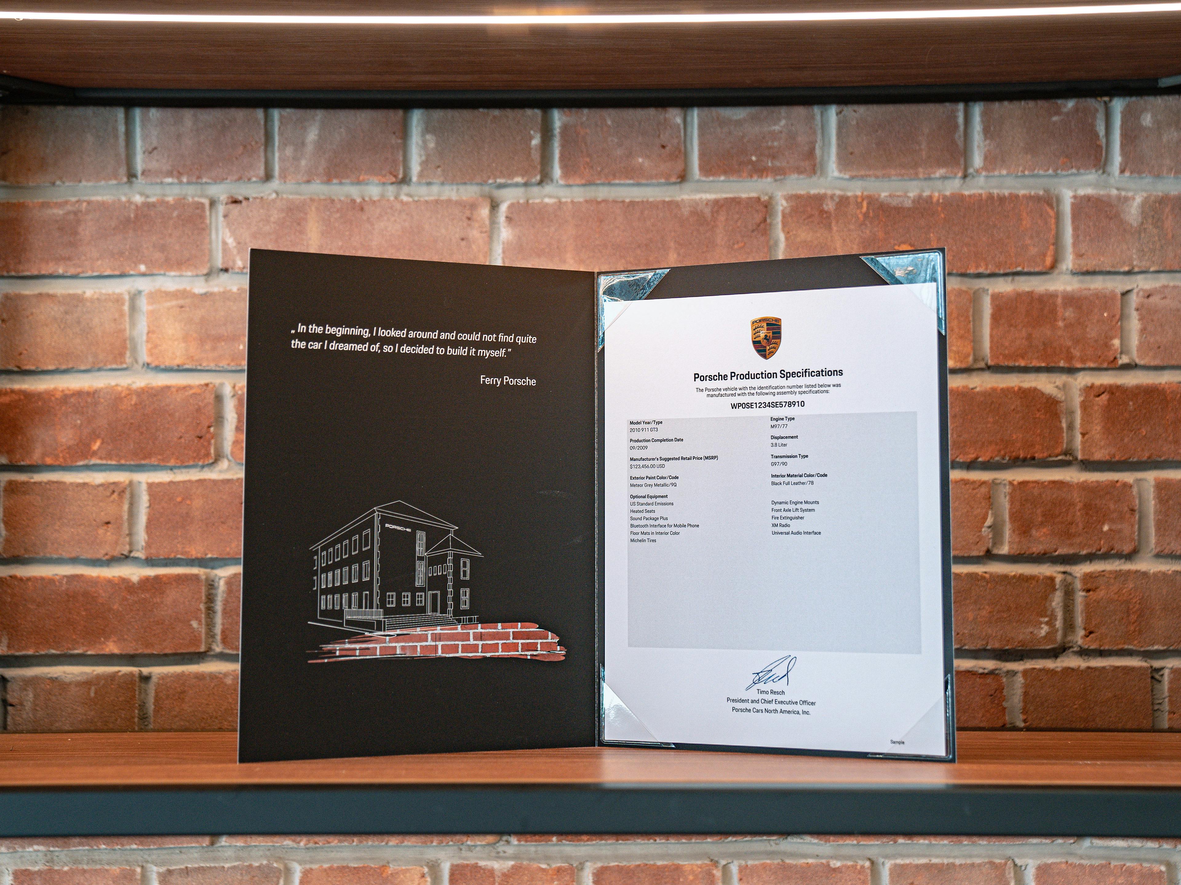 An example of the Porsche Production Specification folder sitting on display in front of a brick wall.