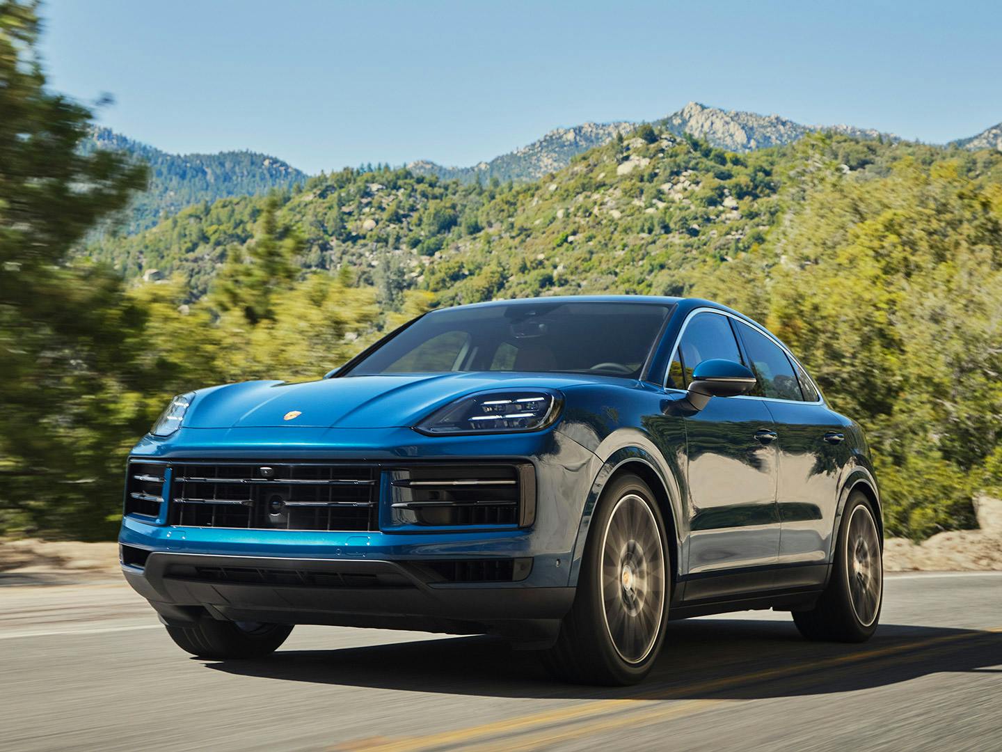 Un Porsche Cayenne bleu circulant sur une route montagneuse.