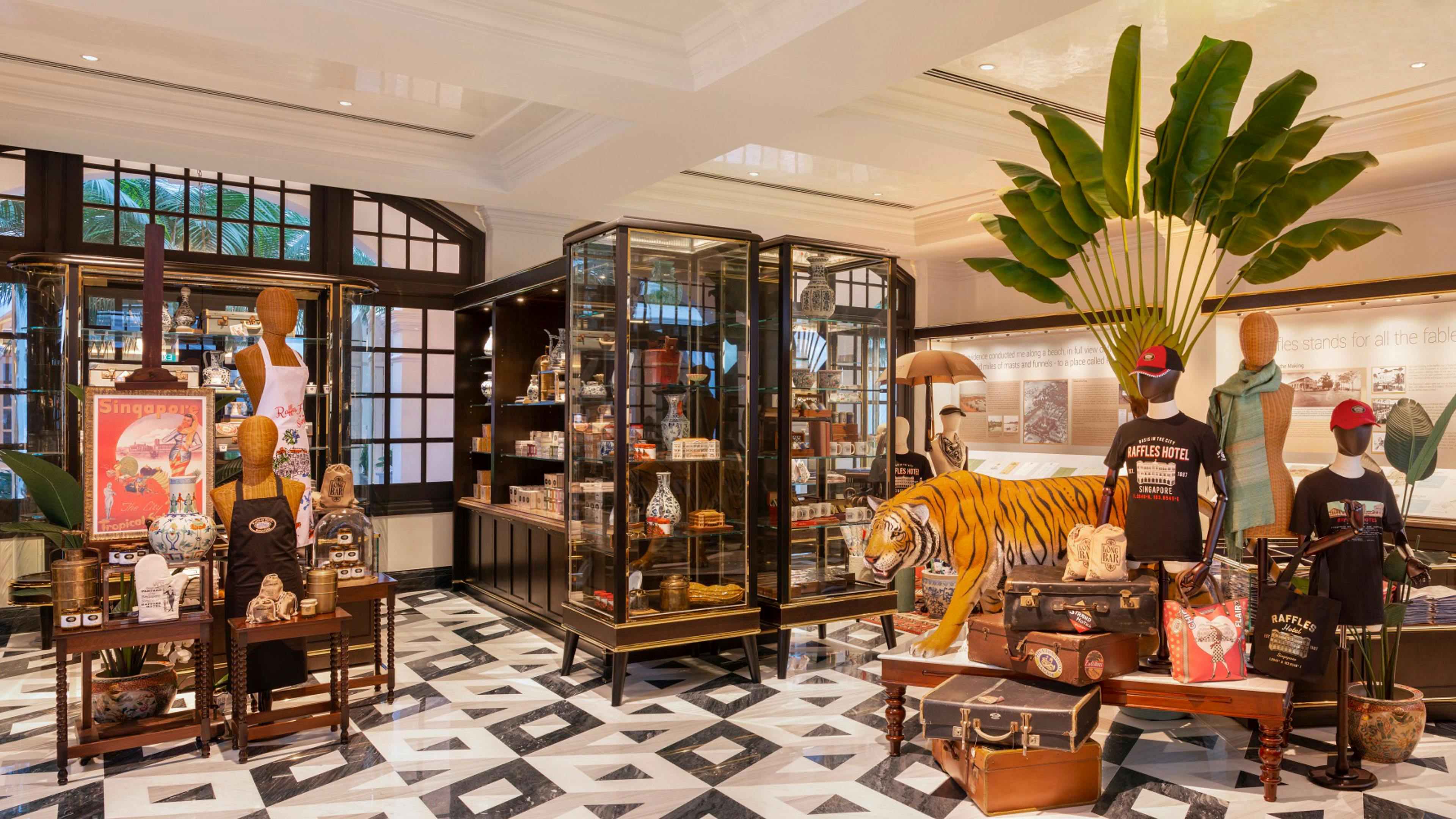 Raffles Hotel Boutique store with display cases of gifts, tiger statue, and Raffles-branded merchandise.