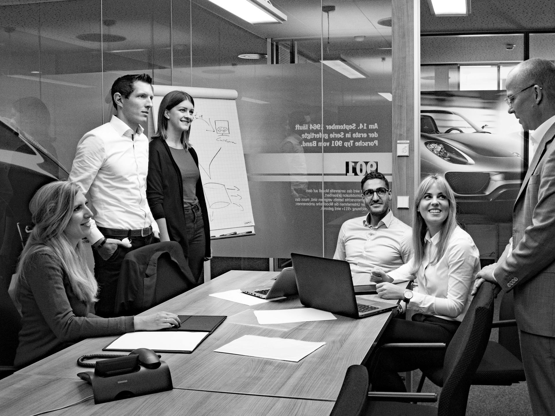 Black-and-white photo: Porsche employees are gathered at a table in a meeting room .