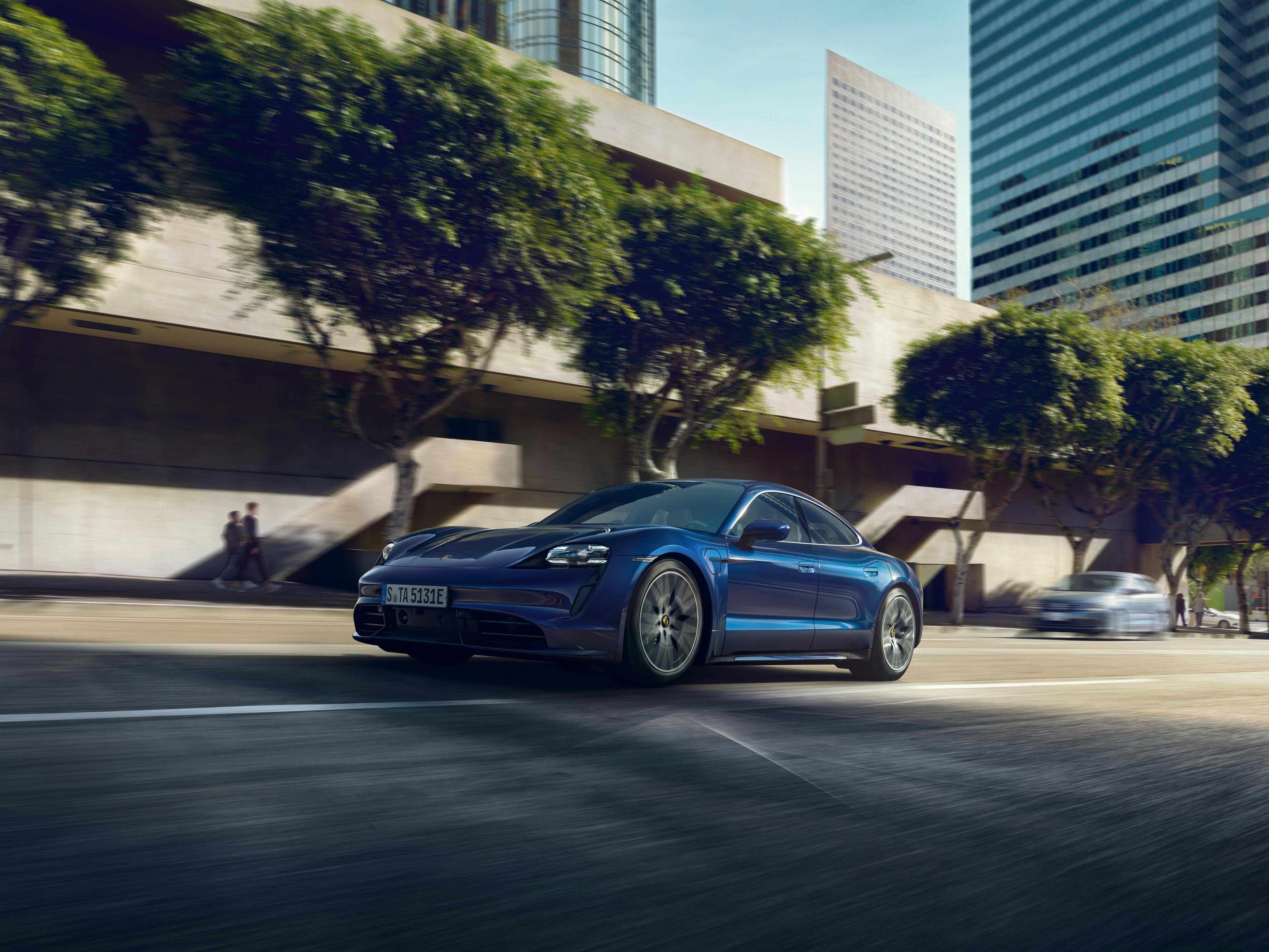 A metallic blue Porsche Taycan driving through a city.