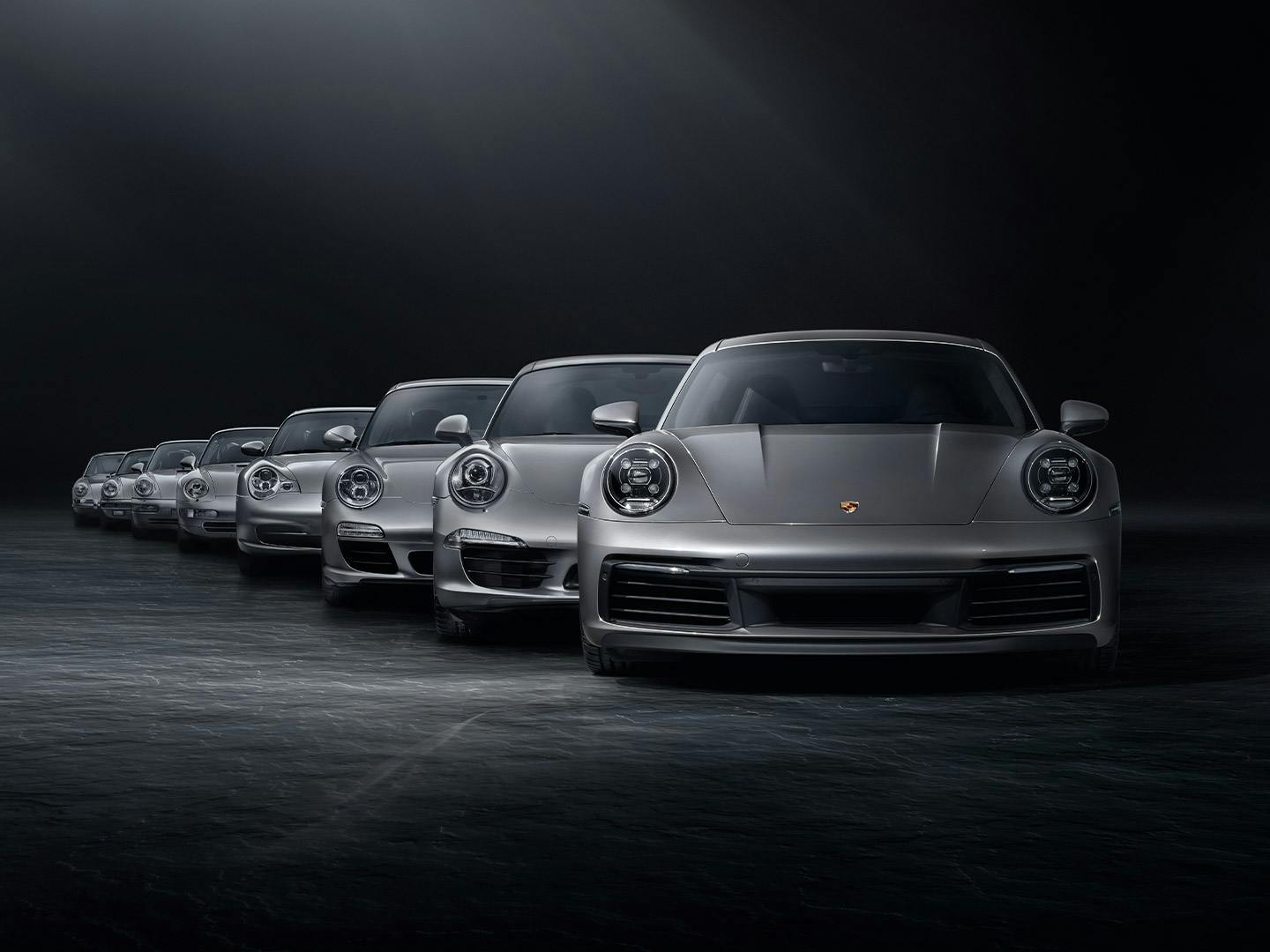 In a black studio, various silver Porsche 911 generation models are lined up in a row.