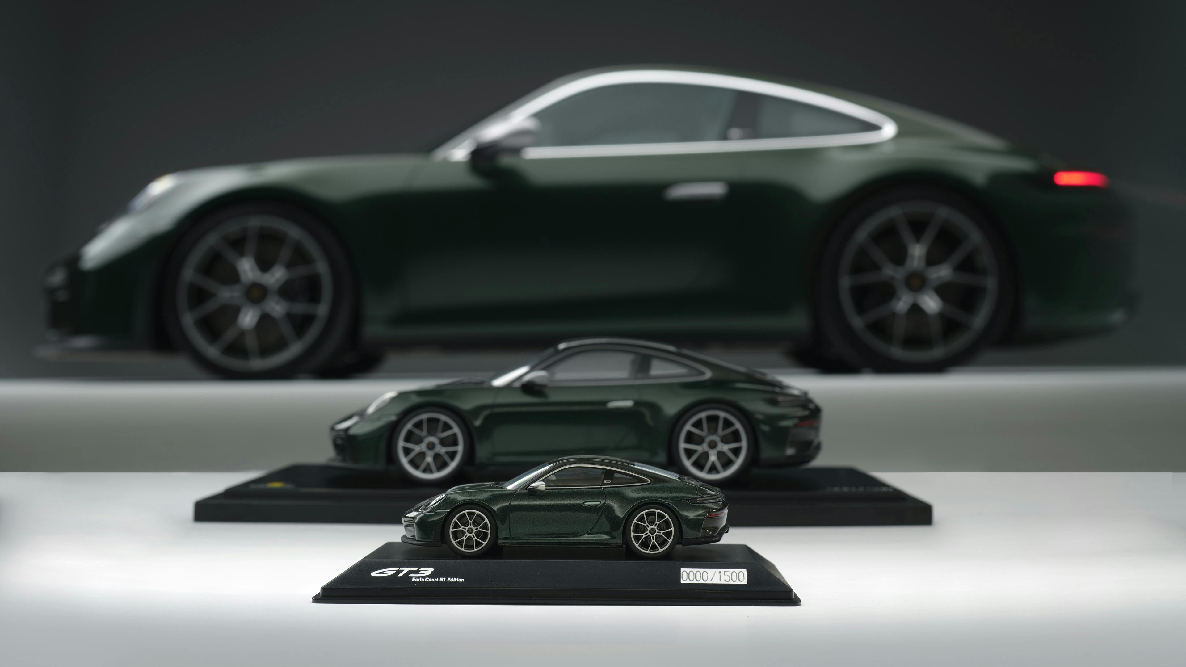 A dark green Porsche 911 shown in side profile, with a matching scale model displayed on a stand beneath it.​
