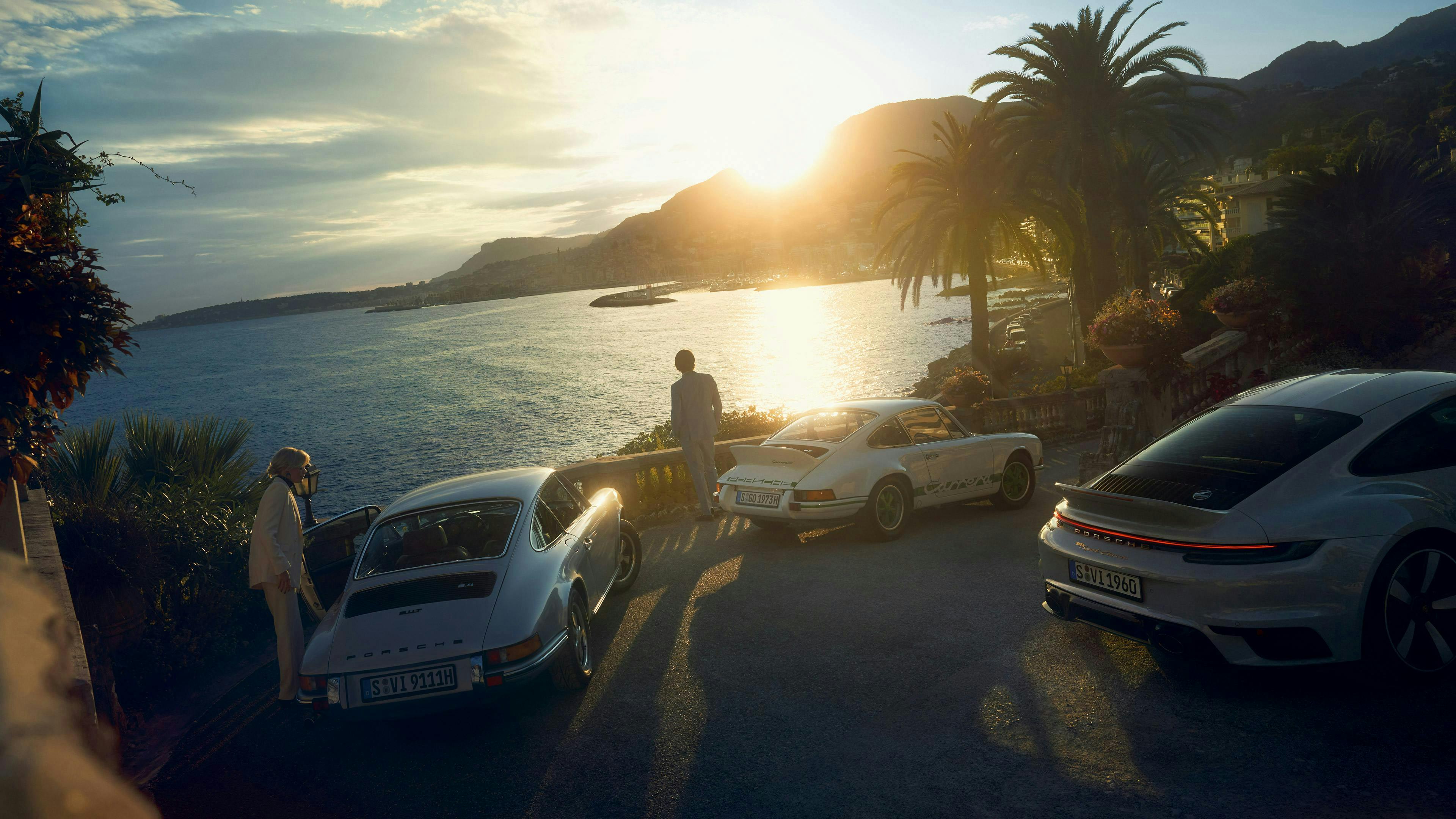 Une Porsche 911 Sport Classic en Gris Sport métallisé roulant sur une route côtière à côté d'une Porsche 911 classique. Vue de l'arrière du véhicule.