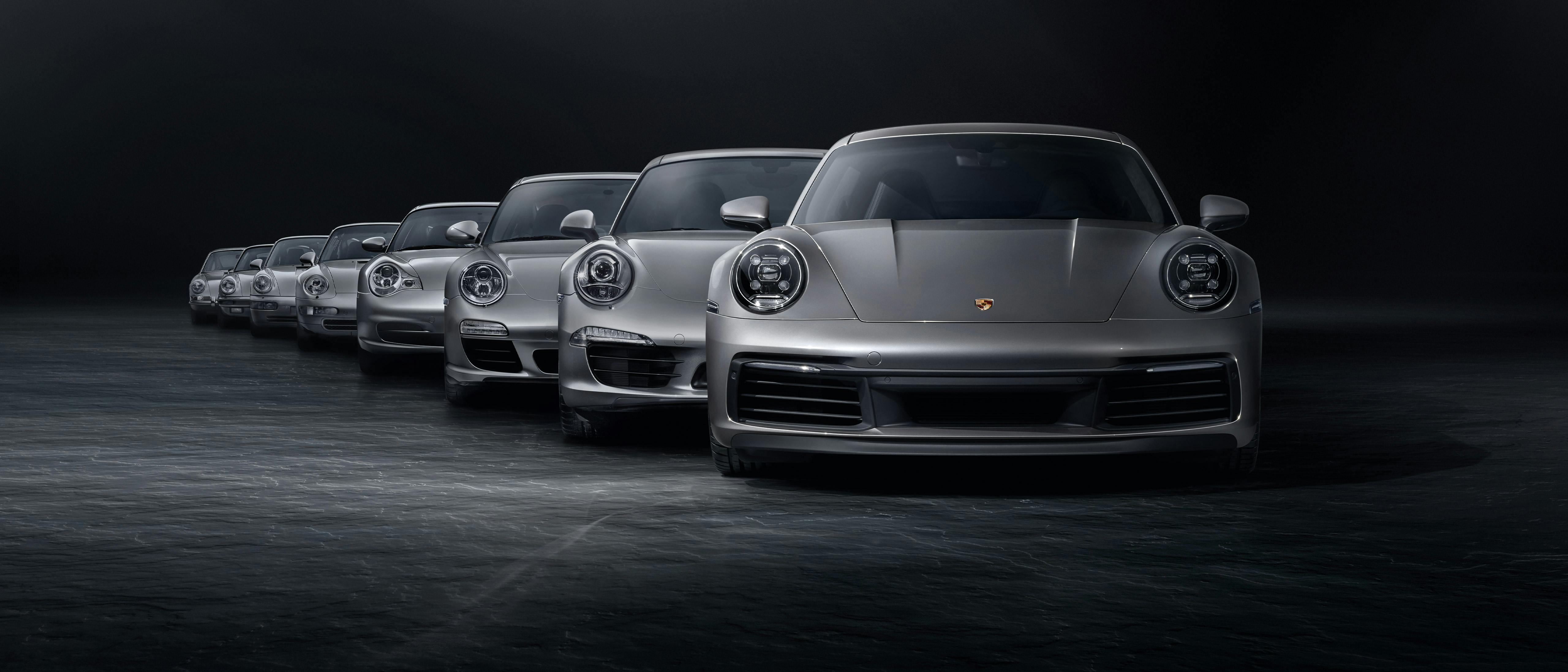 In a Black studio, eight Silver 911 Carrera models are arranged one after the other from the rear and illuminated with a beam of light.