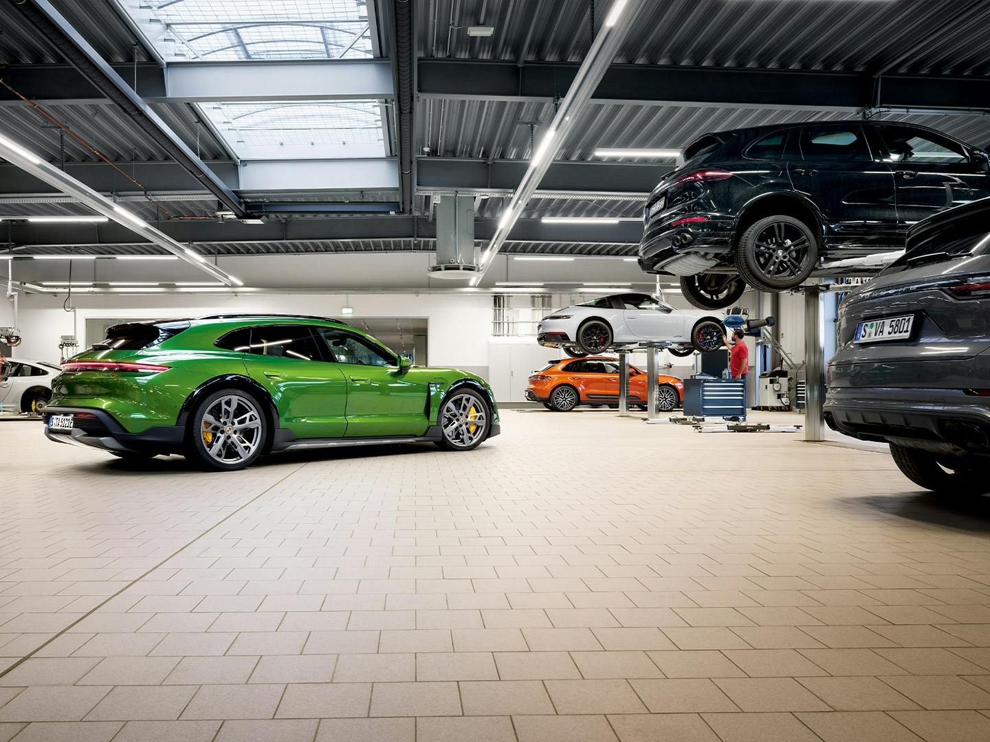A green Porsche Taycan Turbo S Cross Turismo stands in the centre of the Porsche workshop.