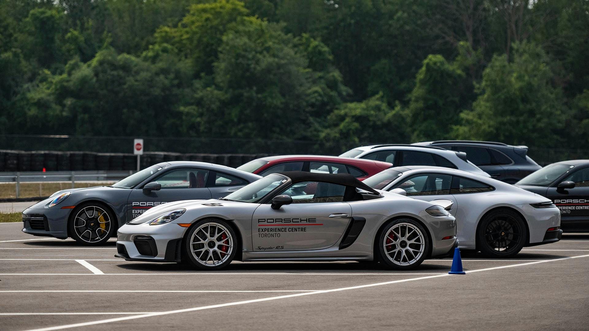 A shot of a couple of Porsche sports cars parked on the side of a circuit, with trees in the background.​