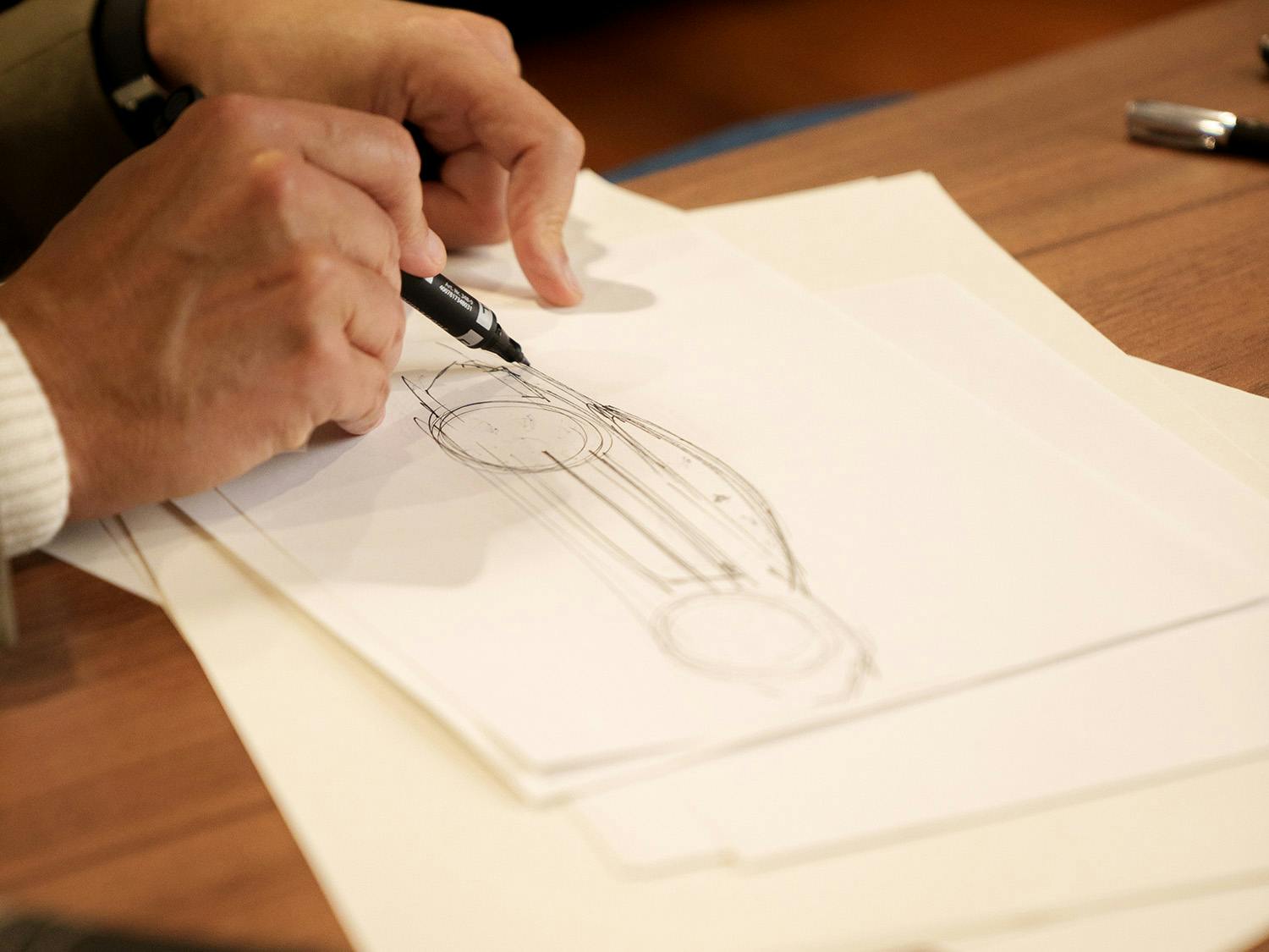 Person drawing a sketch of a car on paper with a pen.
