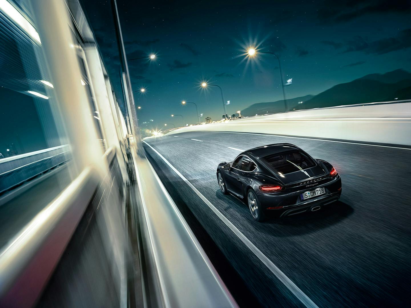 Porsche 718 Cayman nera che guida in autostrada al buio con le luci accese.