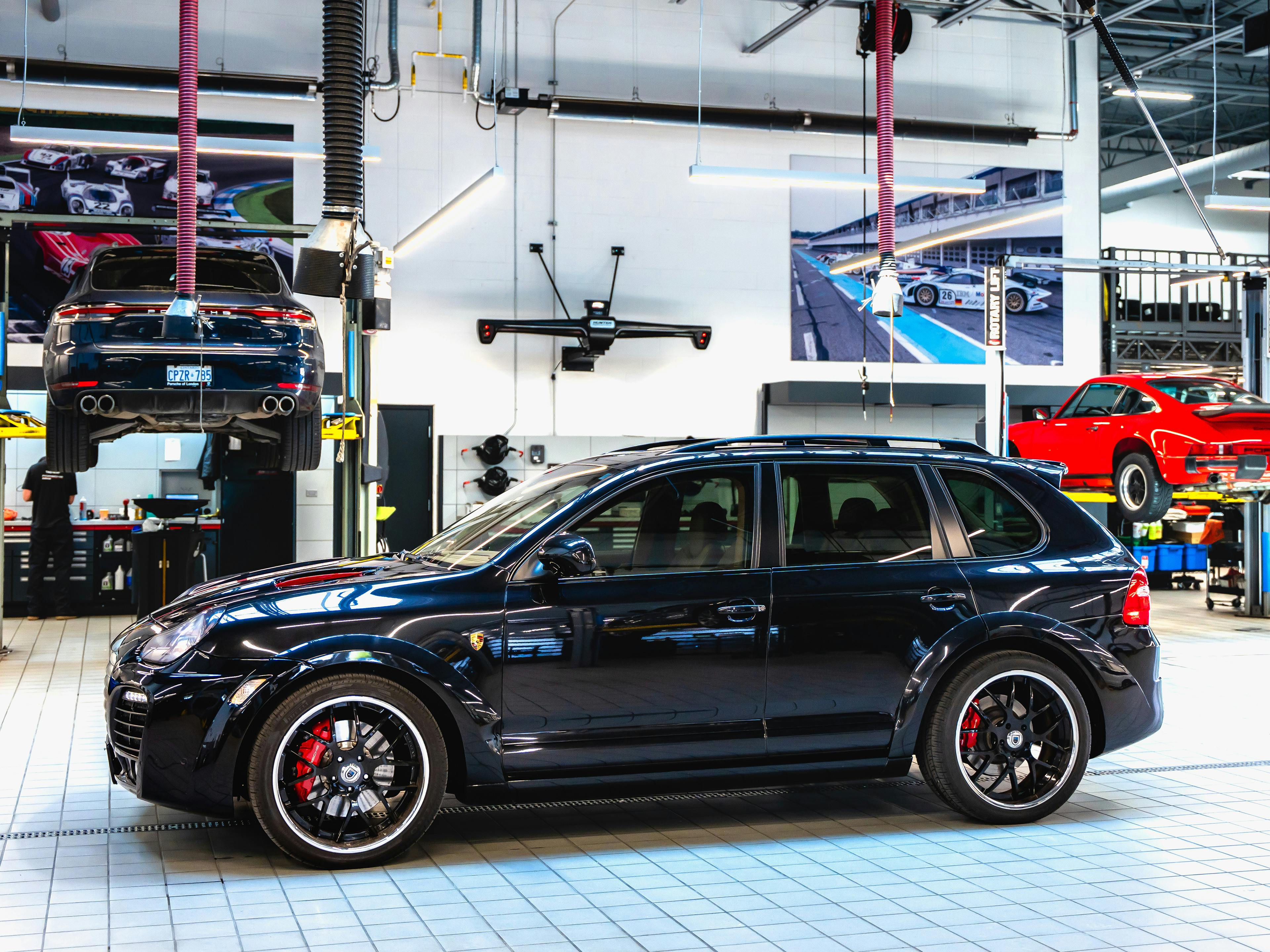 London - A black Porsche Cayenne parked inside a workshop, with other cars being worked on in the service bays.