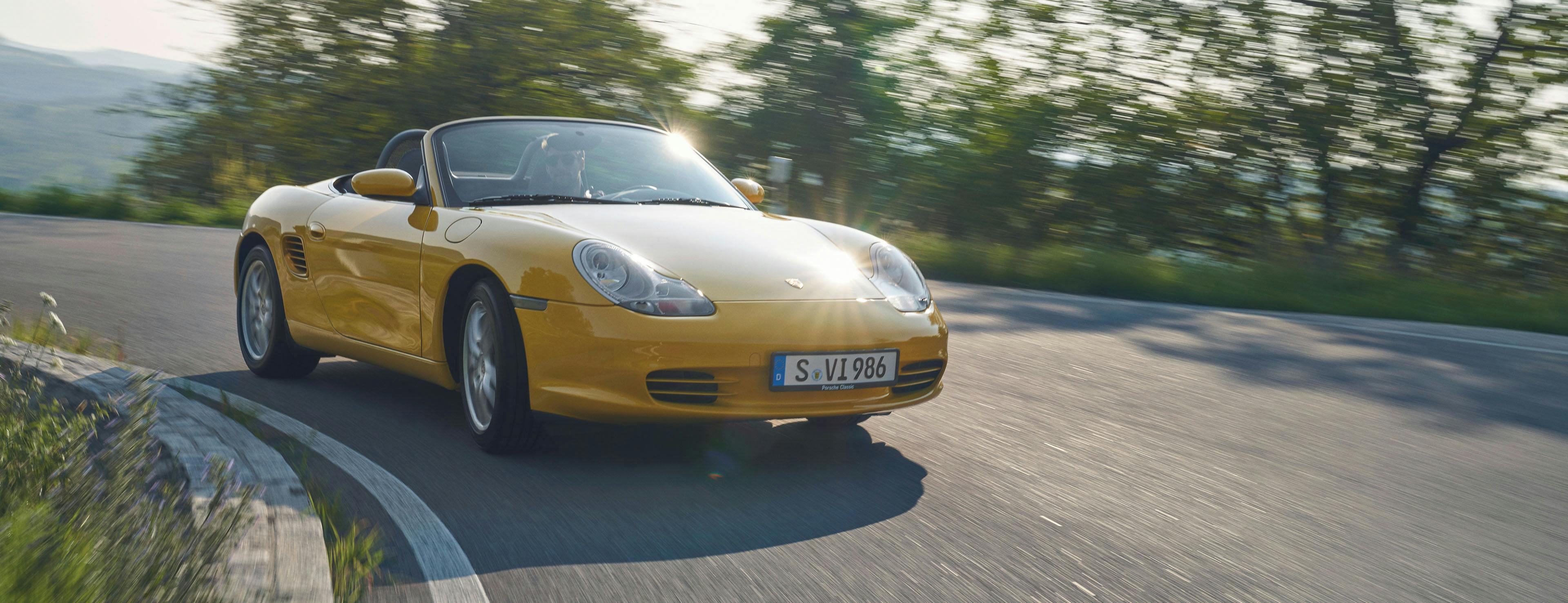 Yellow Porsche Boxster (Type 986) drives along a country road.
