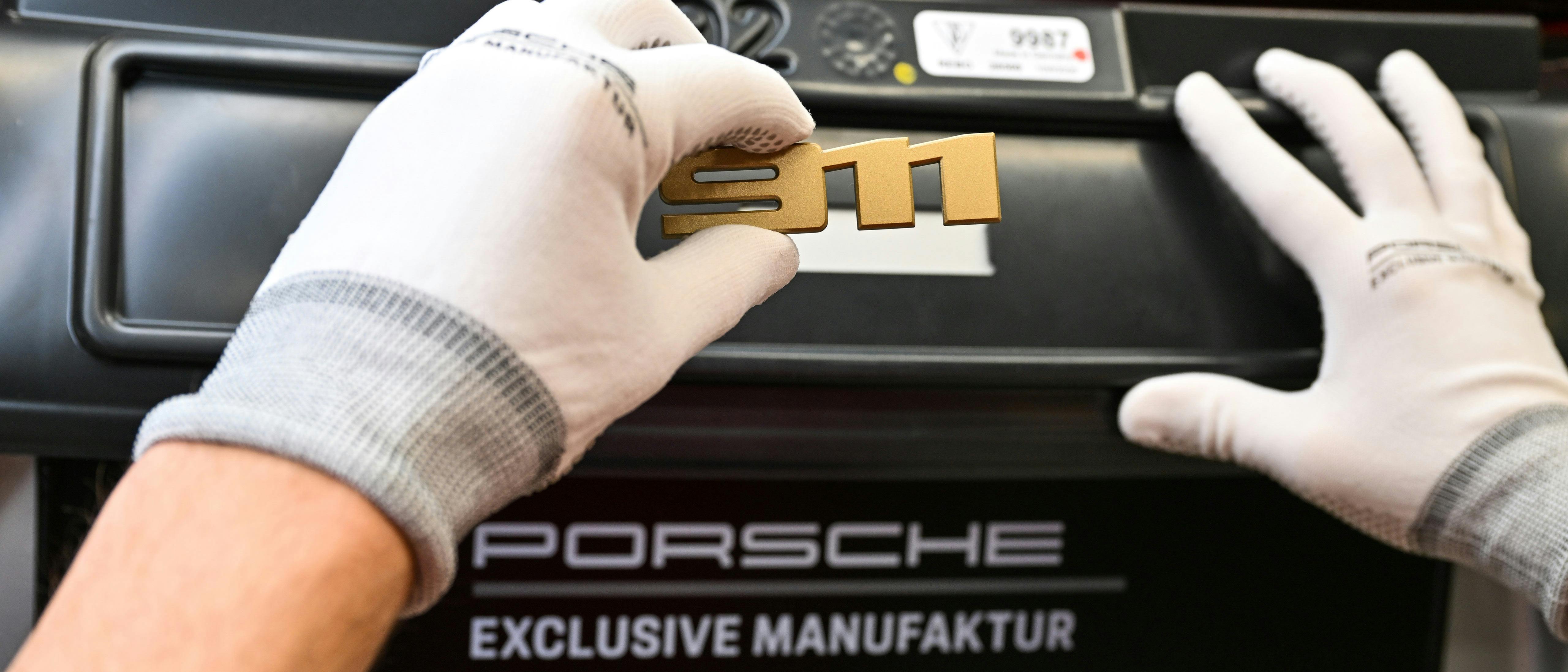 Gloved hands carefully place a 911 emblem on the back of a Porsche.