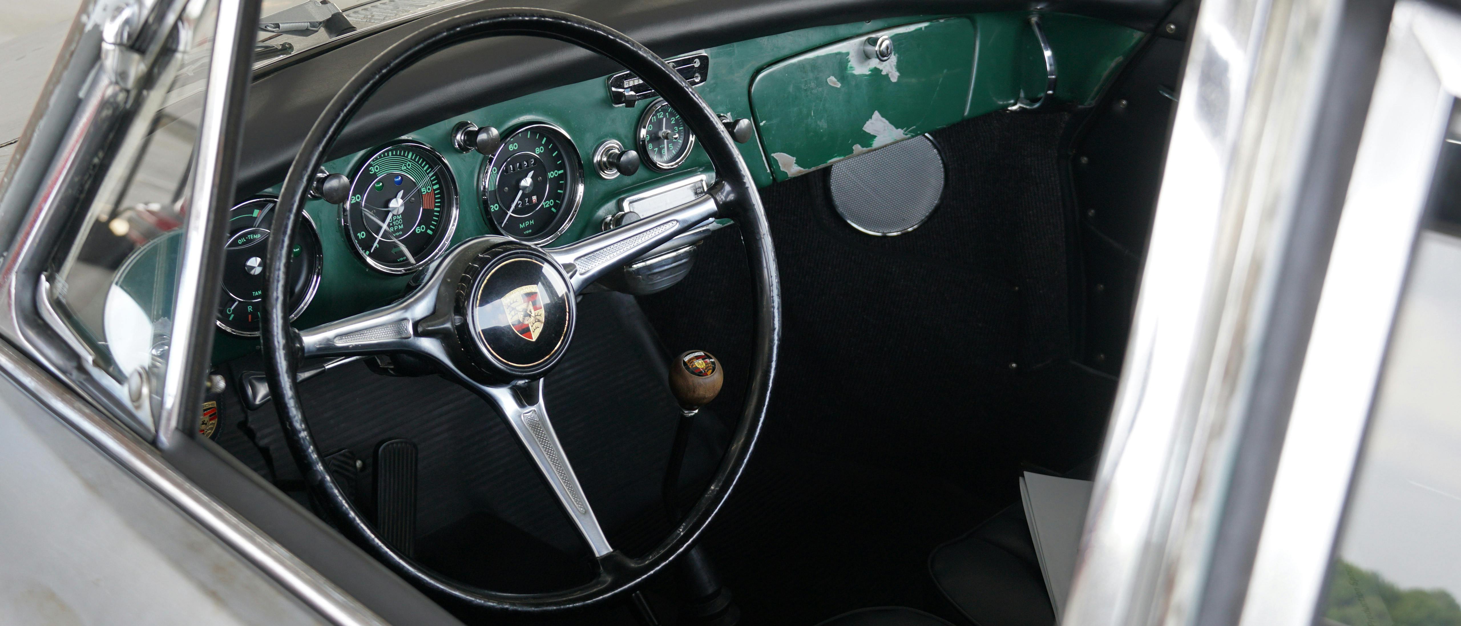 A tight-cropped photo of a silver classic Porsche featuring the steering wheel and dashboard.