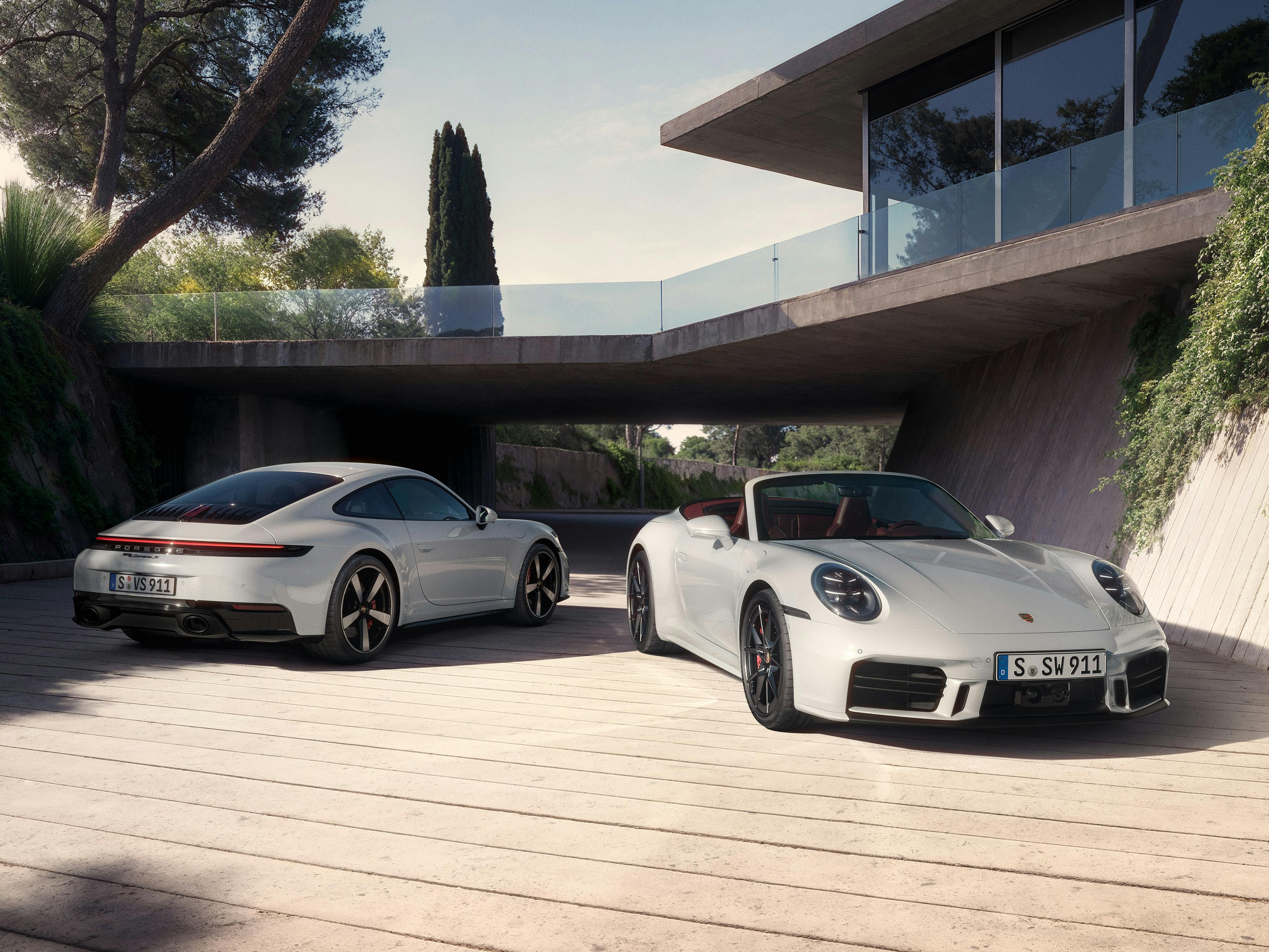 Une Porsche 911 Carrera blanche et une Porsche 911 Cabriolet blanche devant un bâtiment moderne avec des plantations vertes.